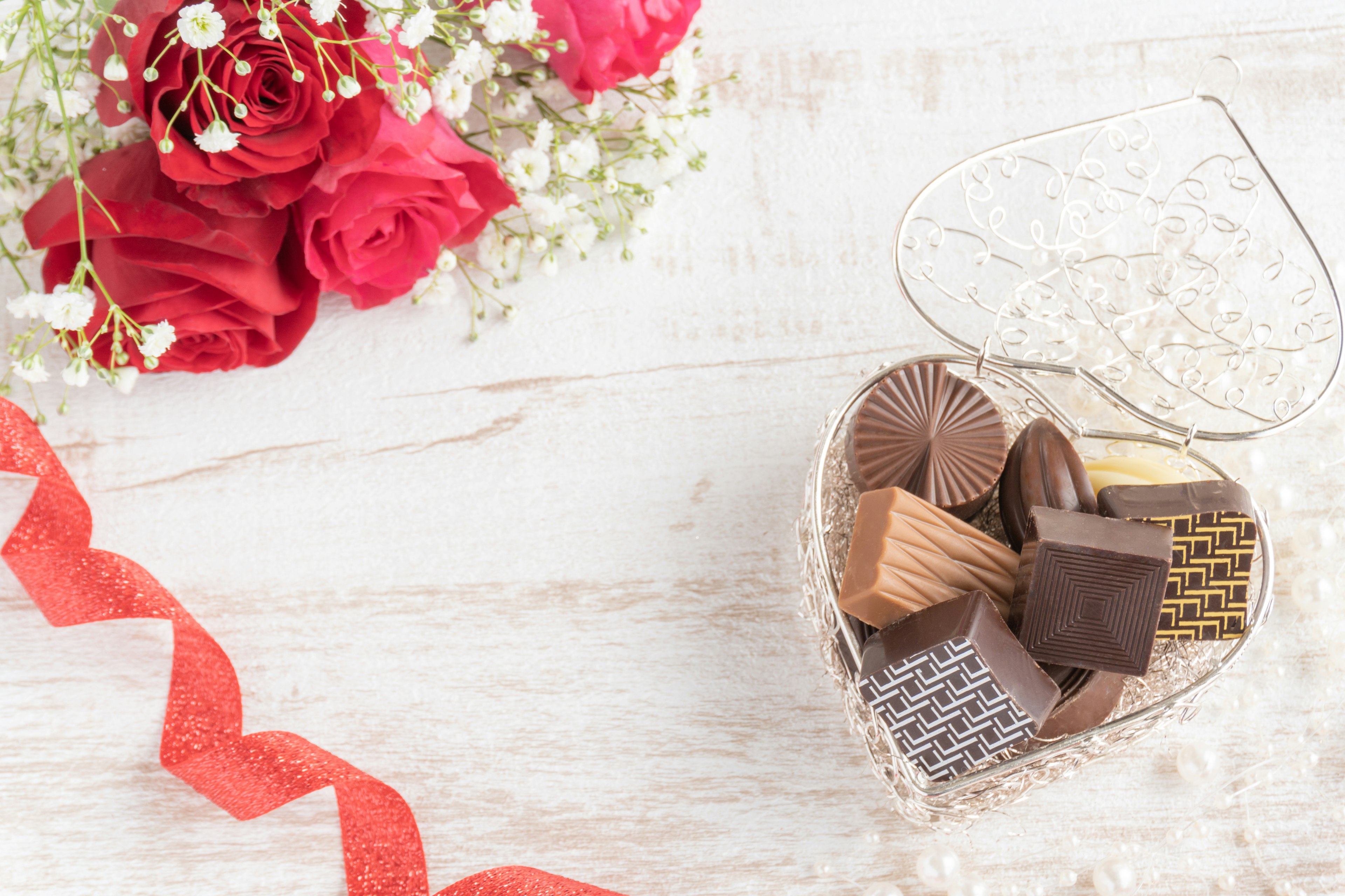 Herzförmige Box gefüllt mit verschiedenen Pralinen und einem Strauß roter Rosen