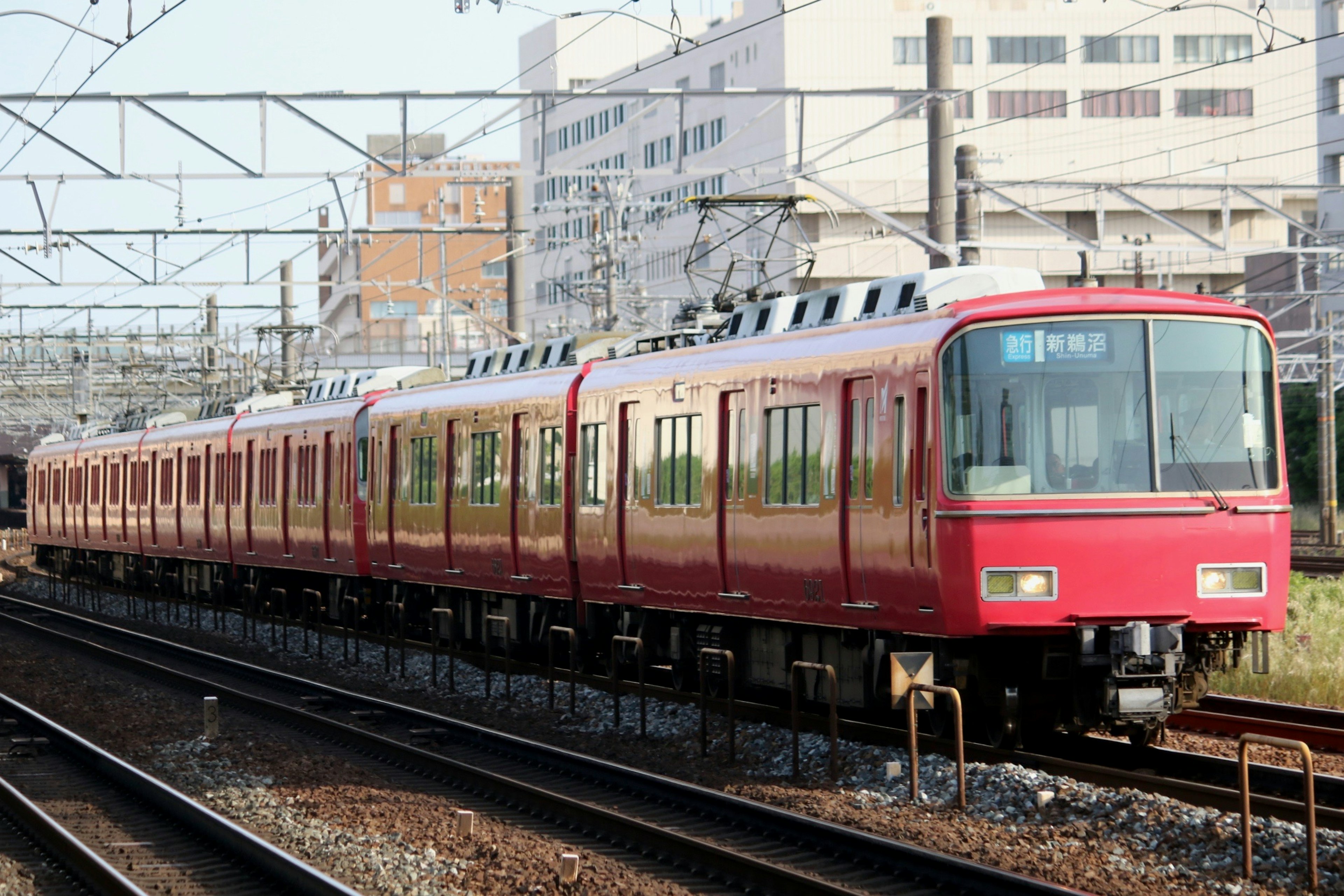 A red train on the tracks with buildings in the background