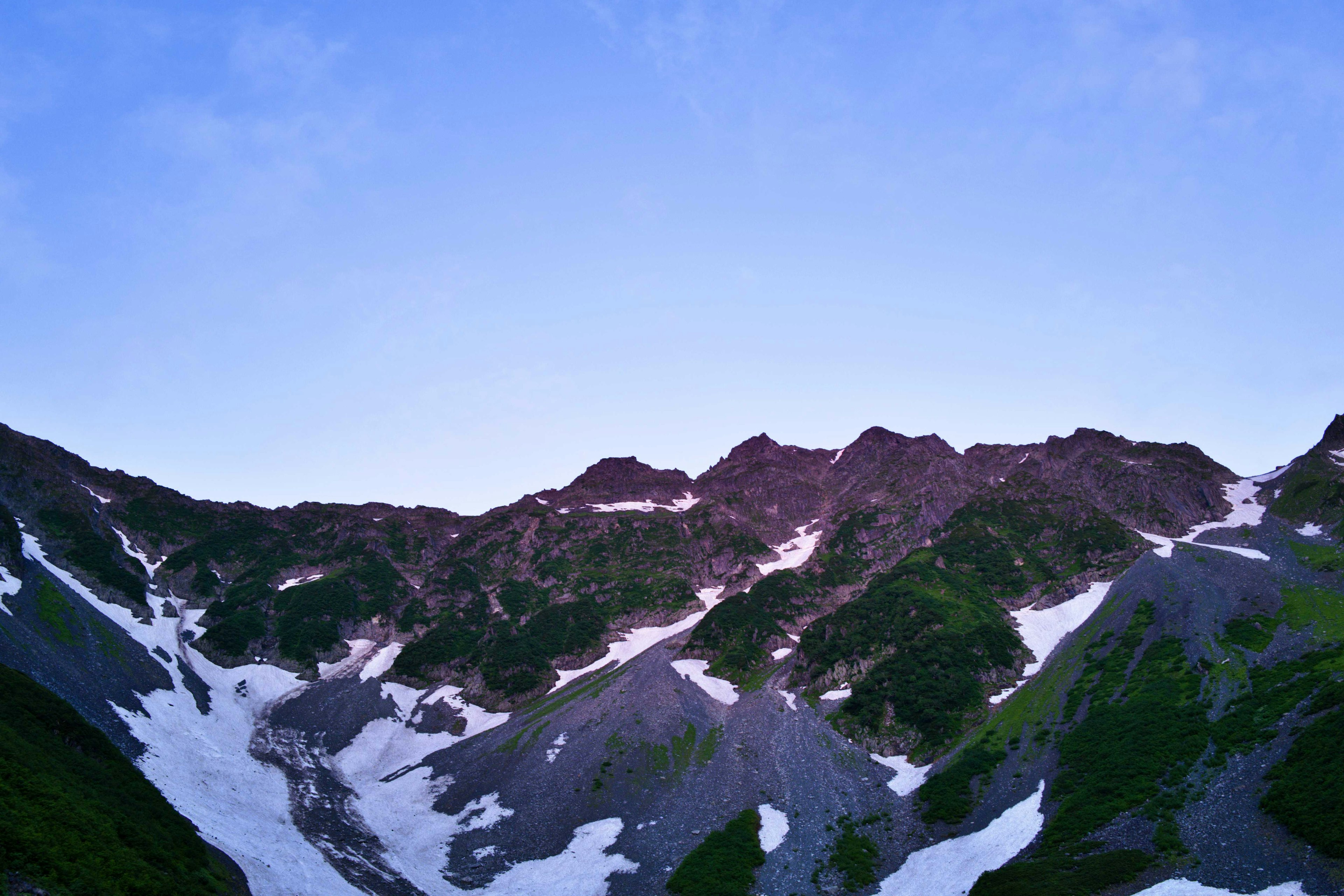 Beeindruckende Landschaft von schneebedeckten Bergen mit grünen Hängen