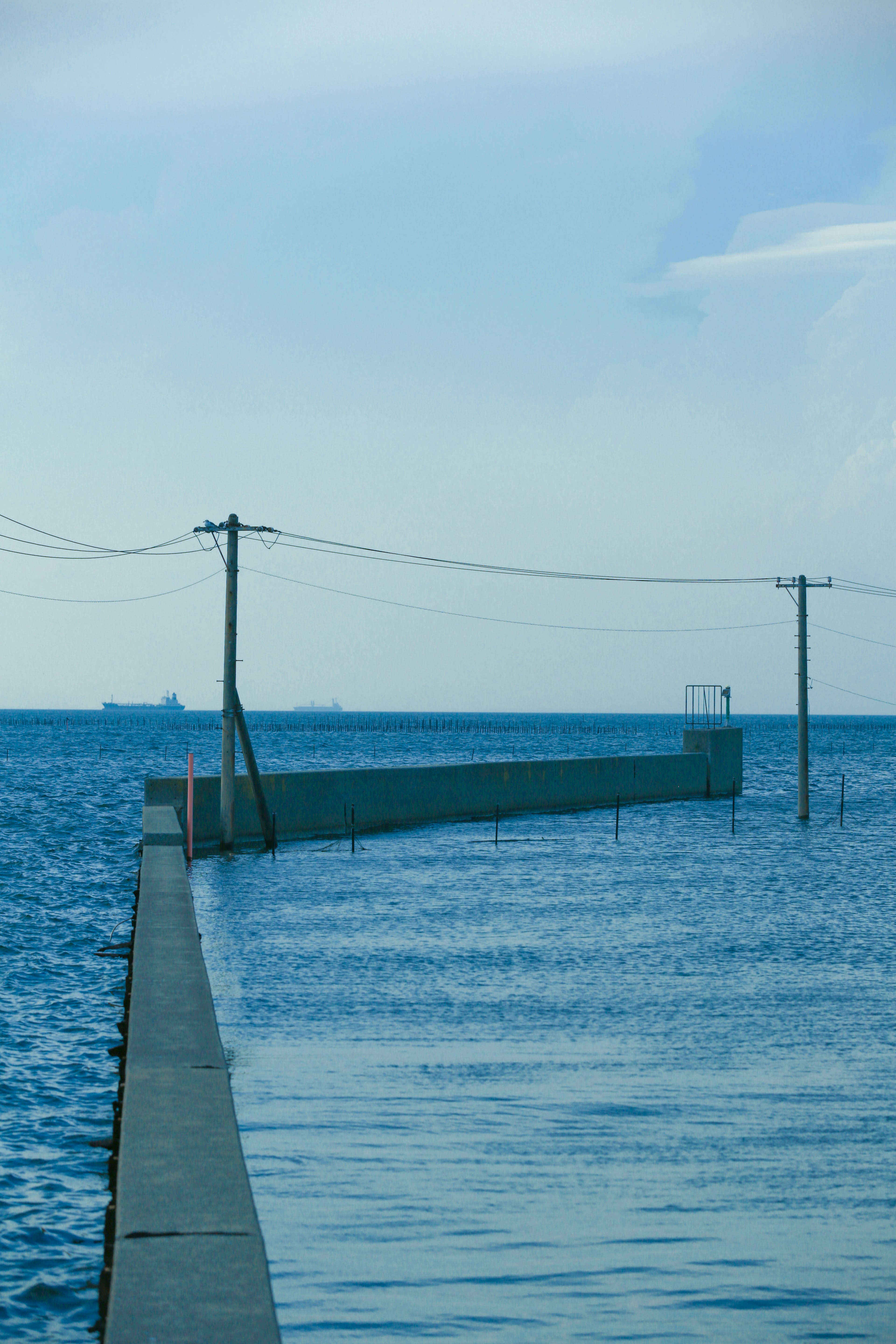 Untergegangener Pier und Strommasten vor blauem Meer und Himmel