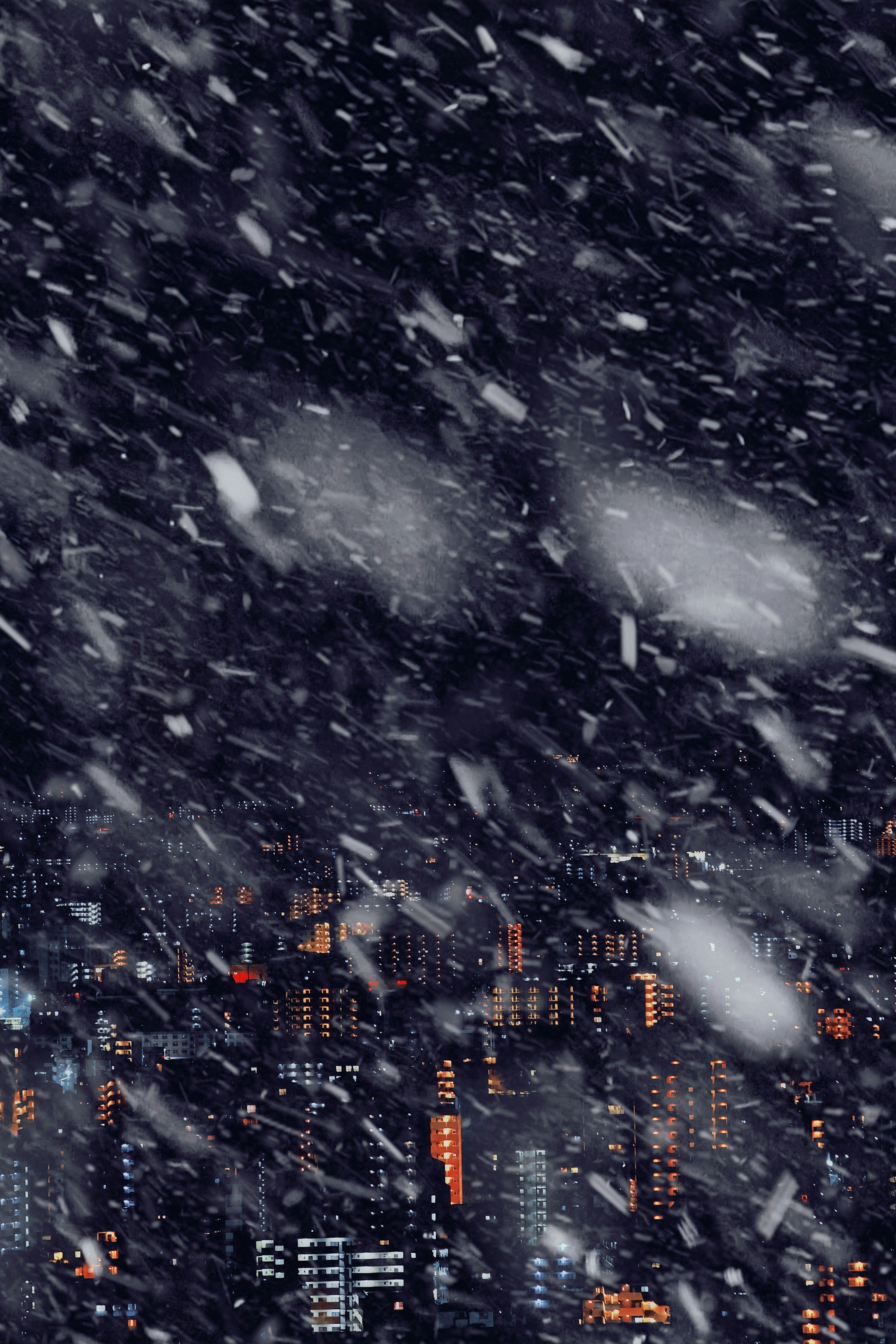 Snowy night cityscape with illuminated buildings and falling snow