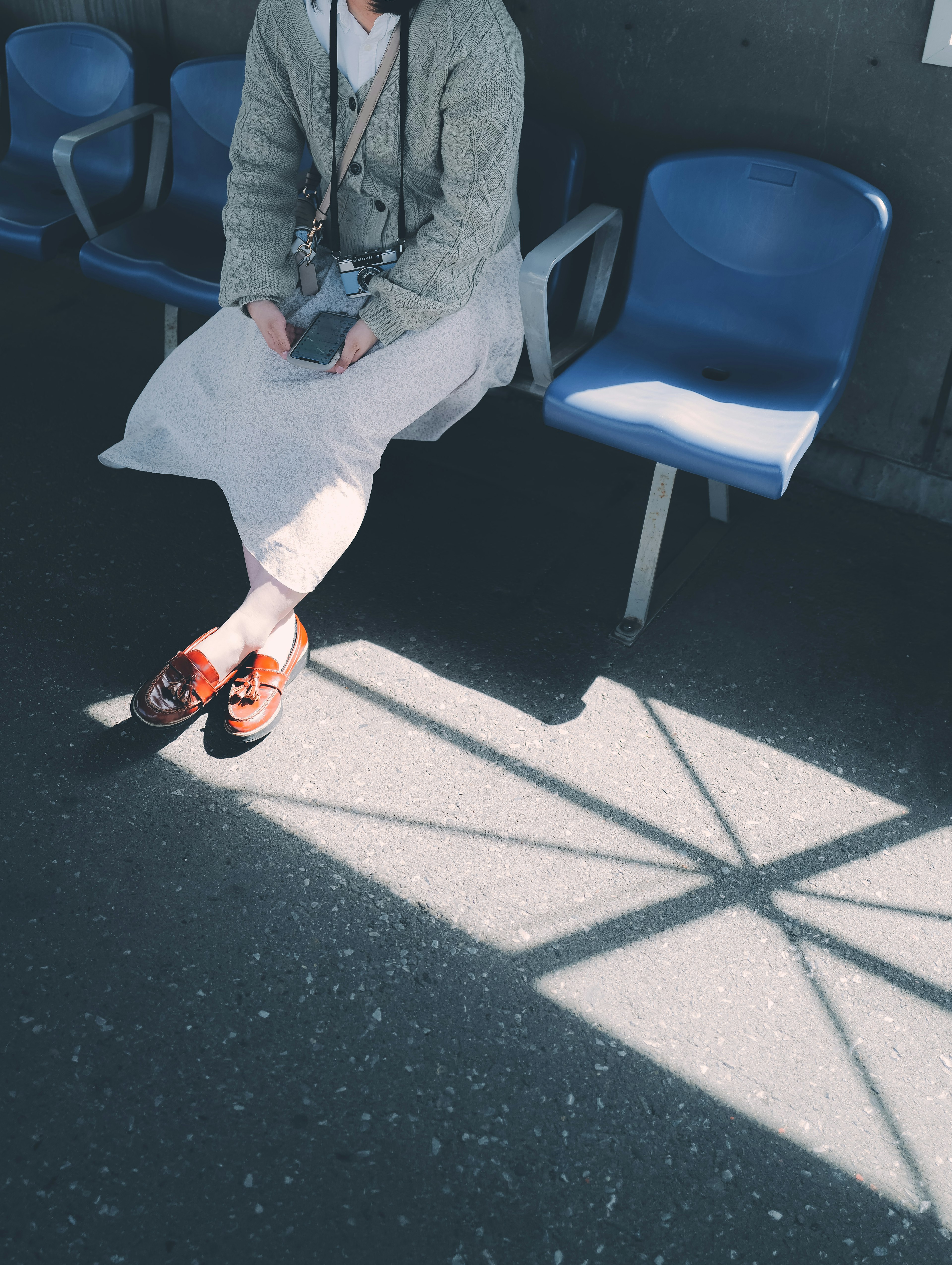 Mujer sentada con zapatos marrones en sillas azules proyectando sombras