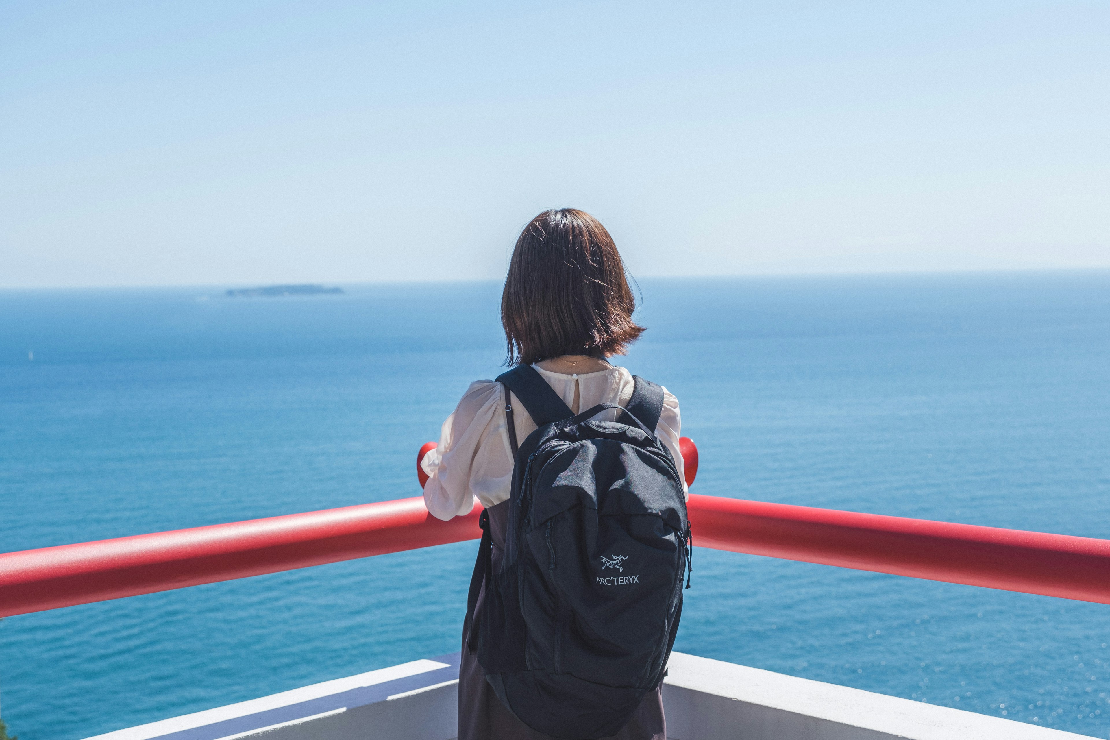 Femme regardant la mer bleue avec une rambarde rouge