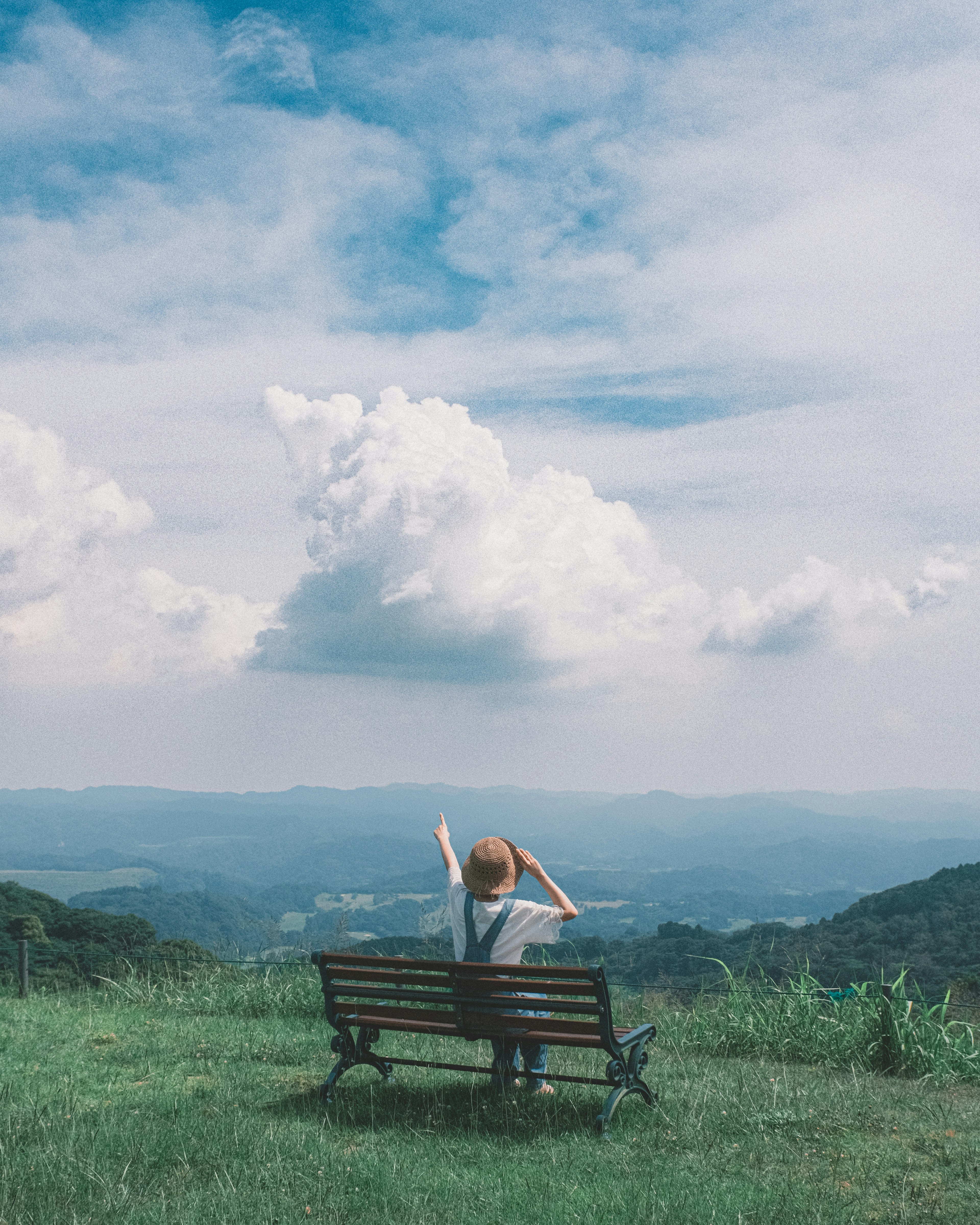 Personne assise sur un banc avec les bras levés sous un ciel bleu et des nuages