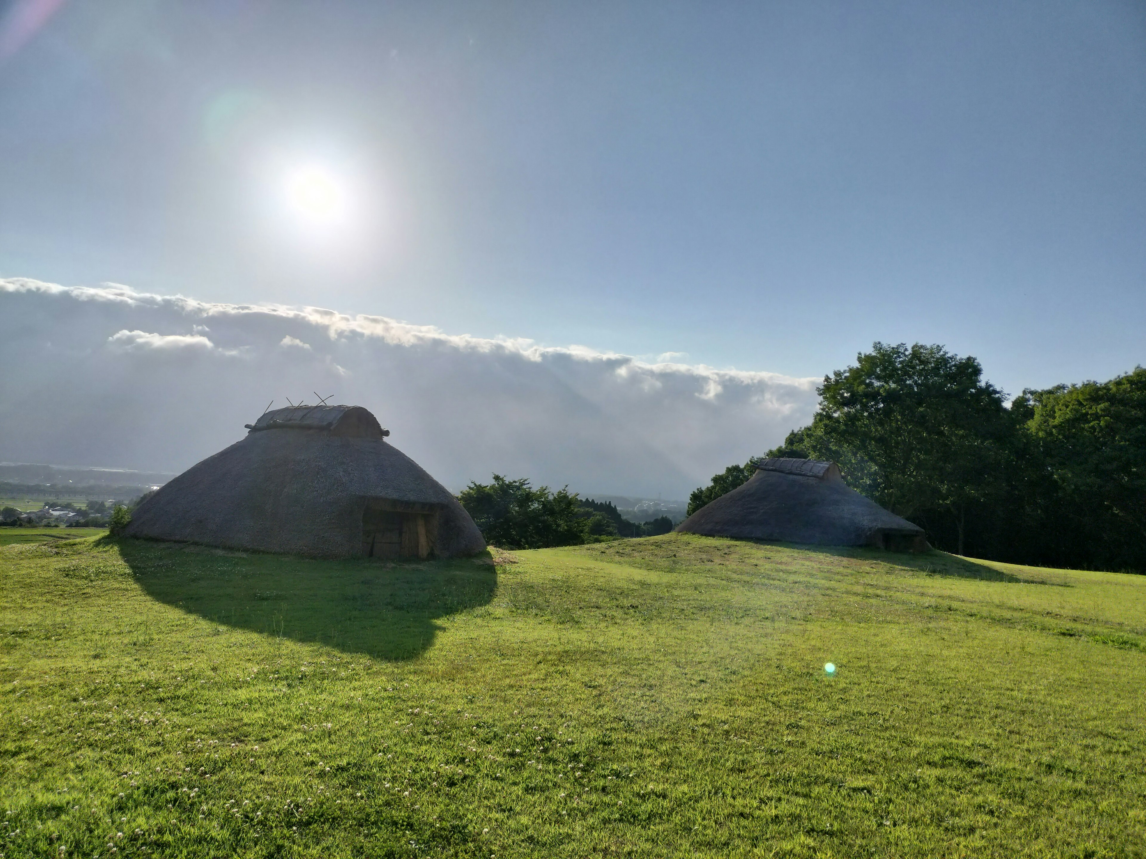 Zwei traditionelle Runddachhäuser auf einer grünen Wiese mit strahlender Sonne