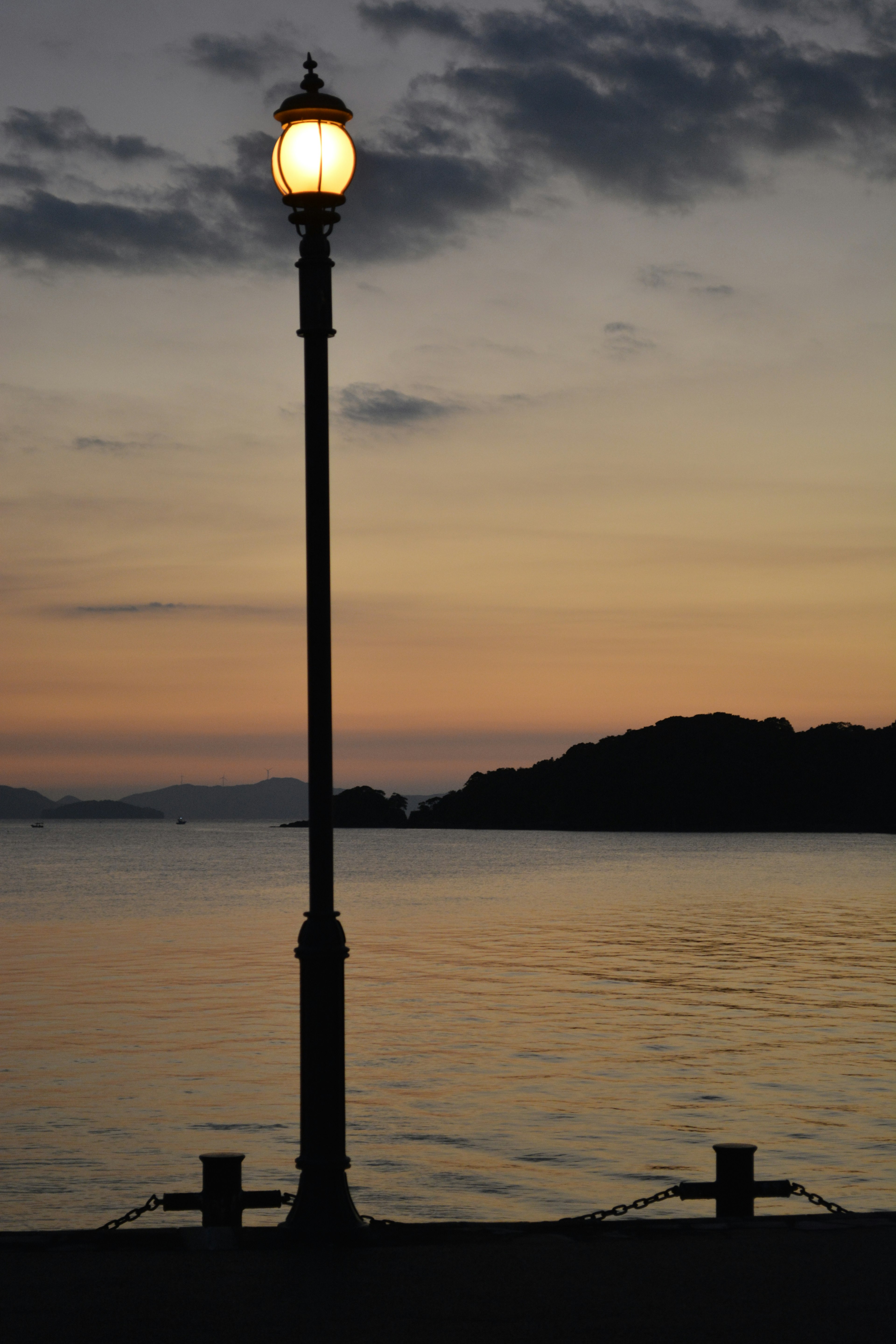 夕暮れの海辺に立つ街灯と静かな水面