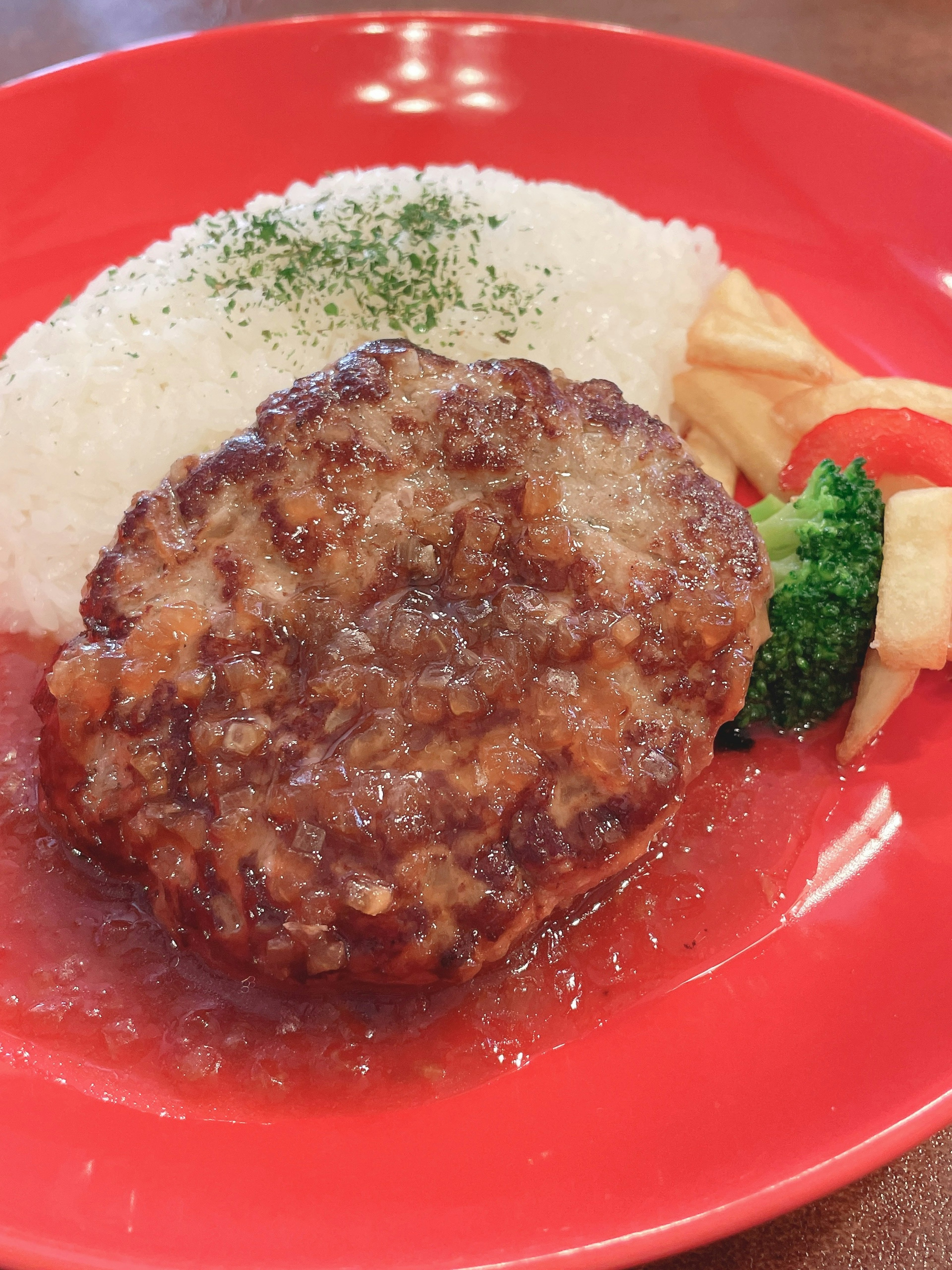 A plate of hamburger steak with rice and vegetables on a red dish