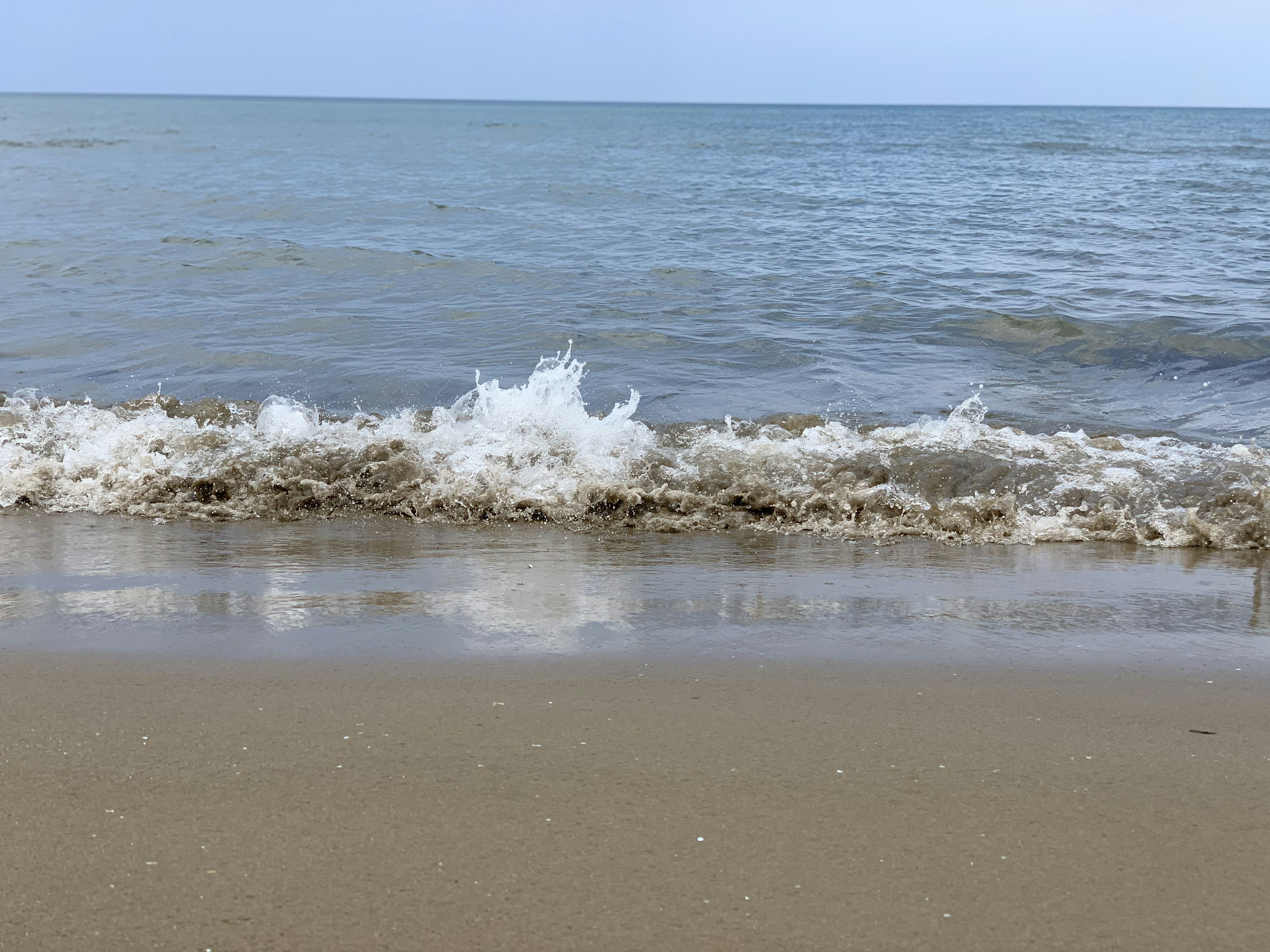 ทิวทัศน์ทะเลสงบและชายหาดทรายคลื่นซัดเข้าหาชายฝั่ง