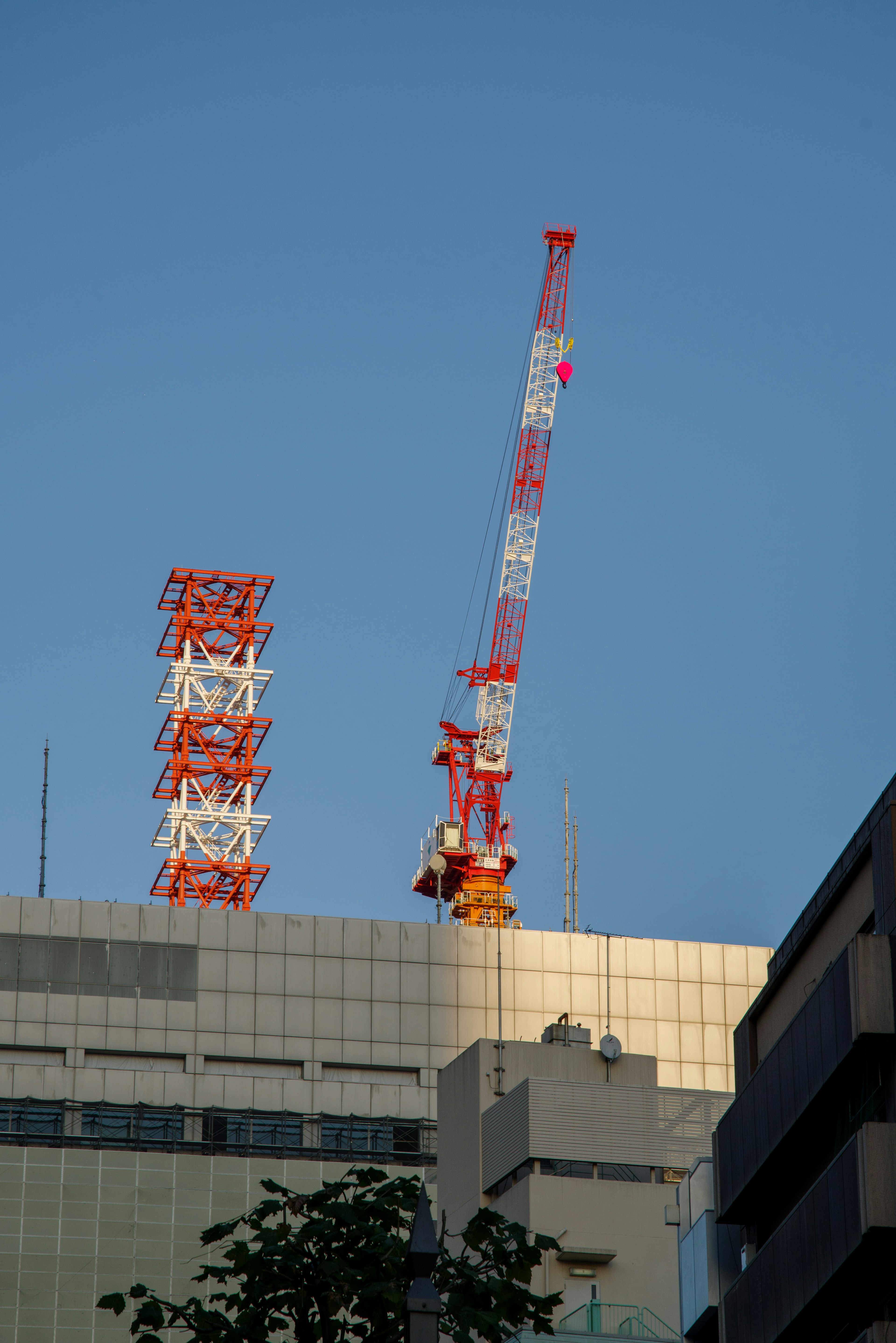 Crane and communication tower on the rooftop of a high-rise building under a clear blue sky