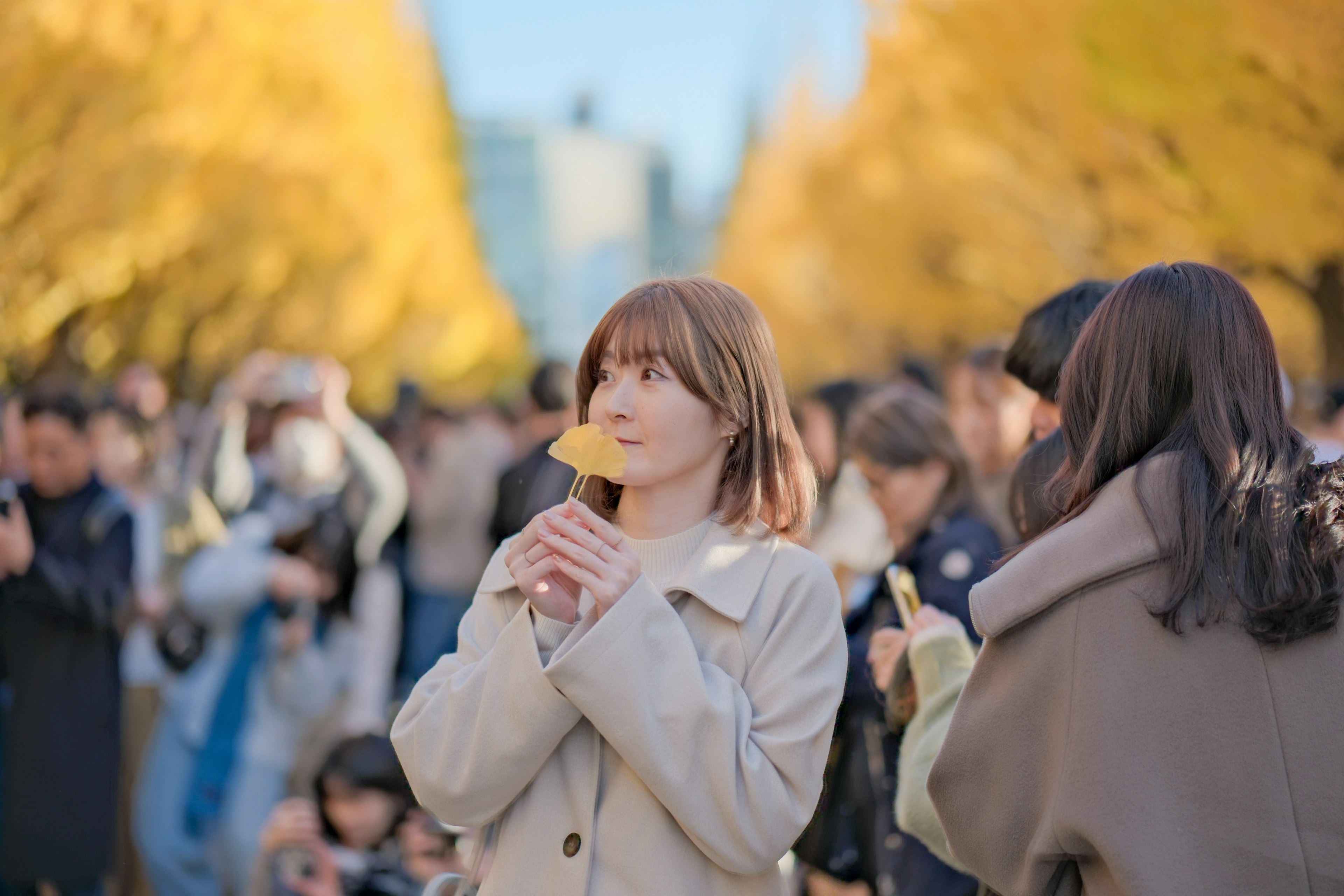 黄色の葉に囲まれた女性が、手に持った食べ物を見つめている