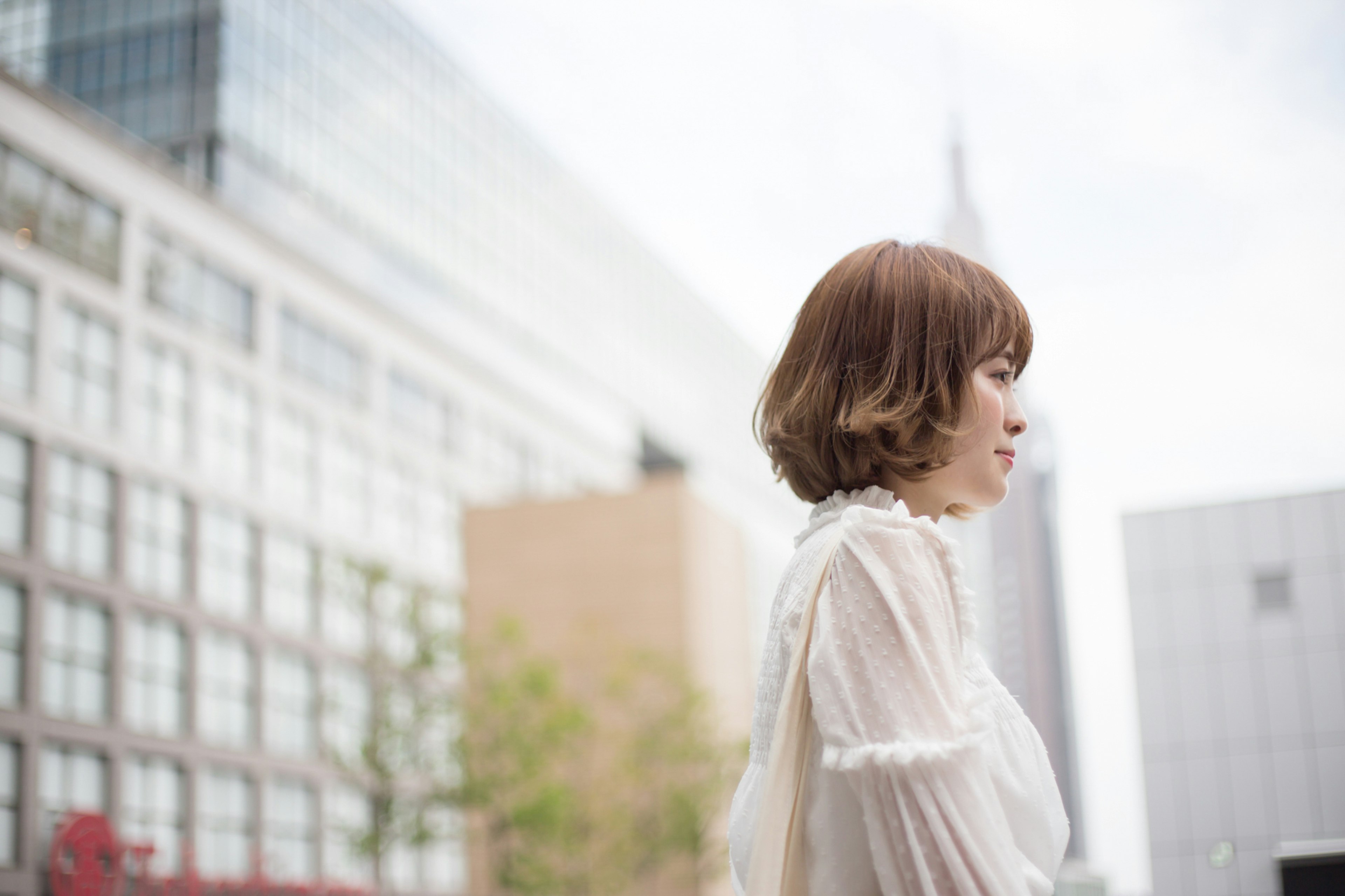 A woman standing sideways in the city with high-rise buildings in the background