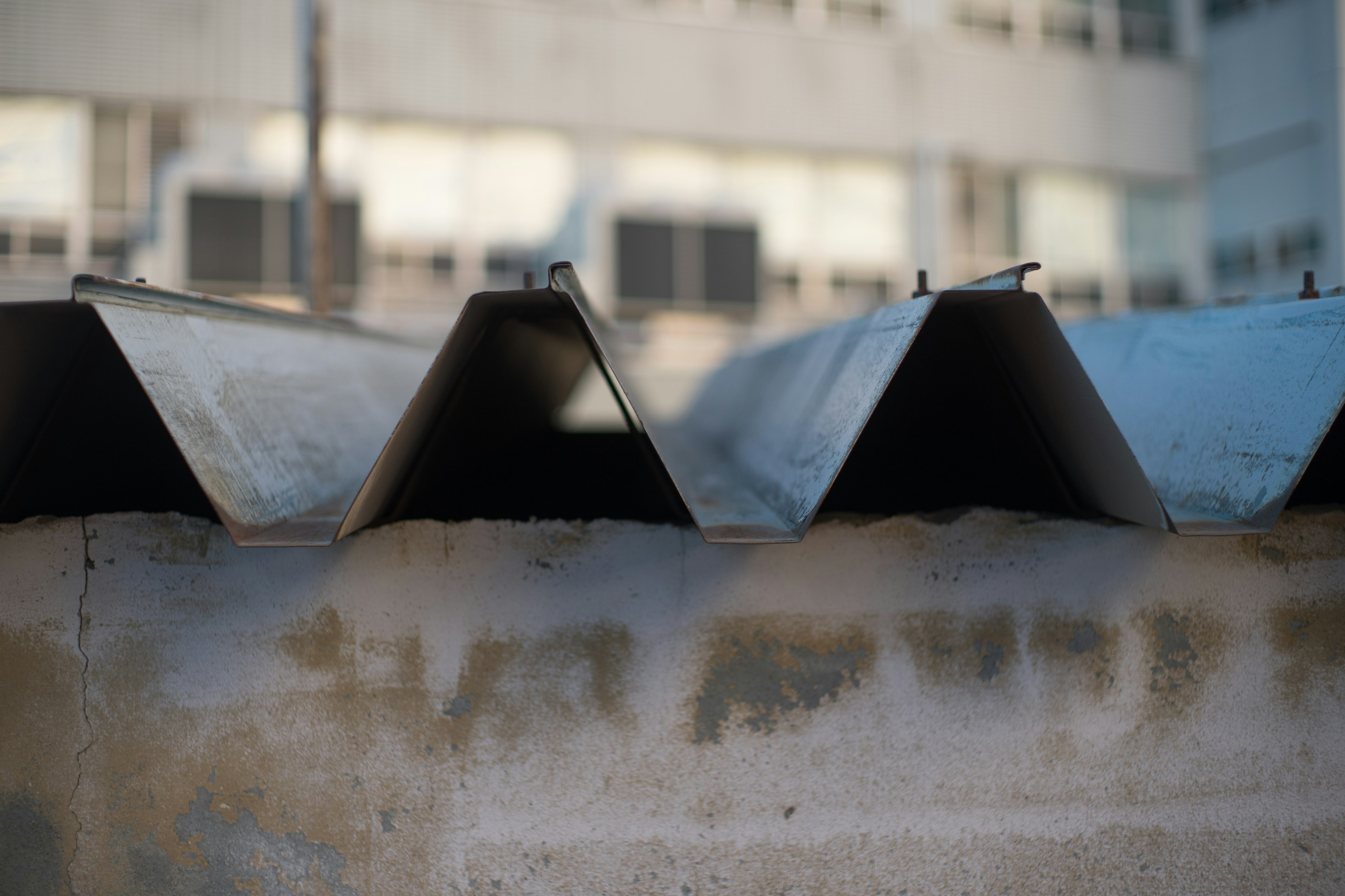 Primer plano de un techo de metal corrugado con ventanas de edificio al fondo