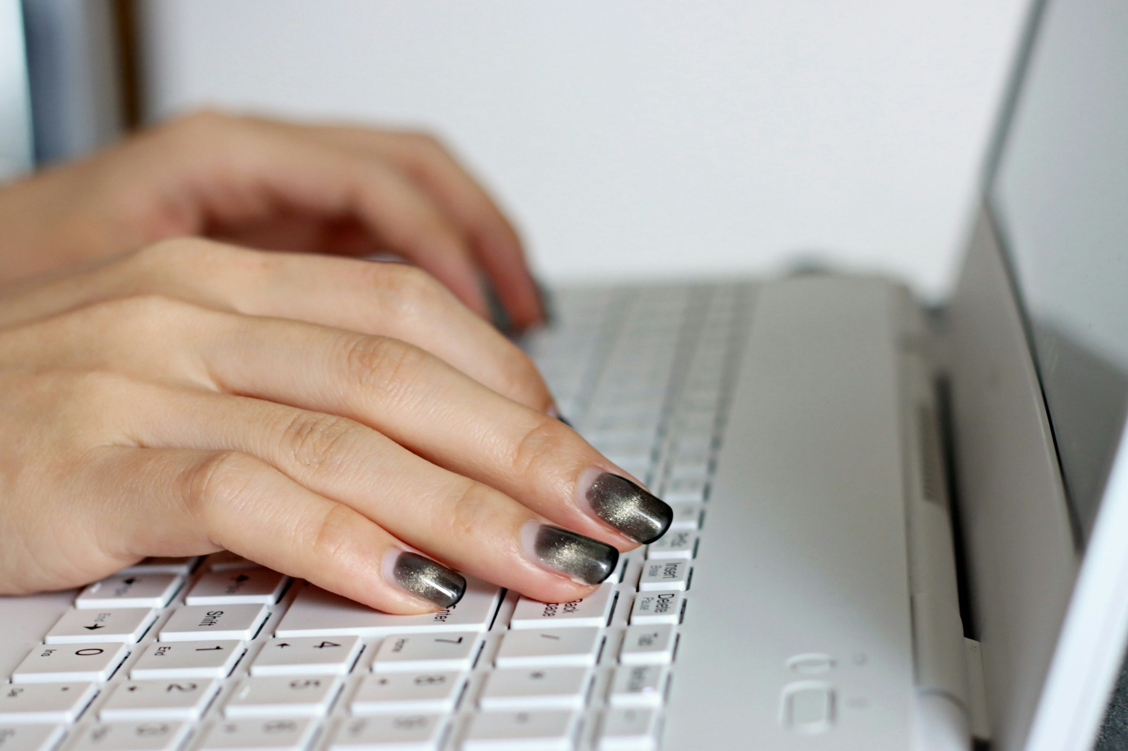 Close-up of hands typing on a laptop keyboard featuring black nail polish