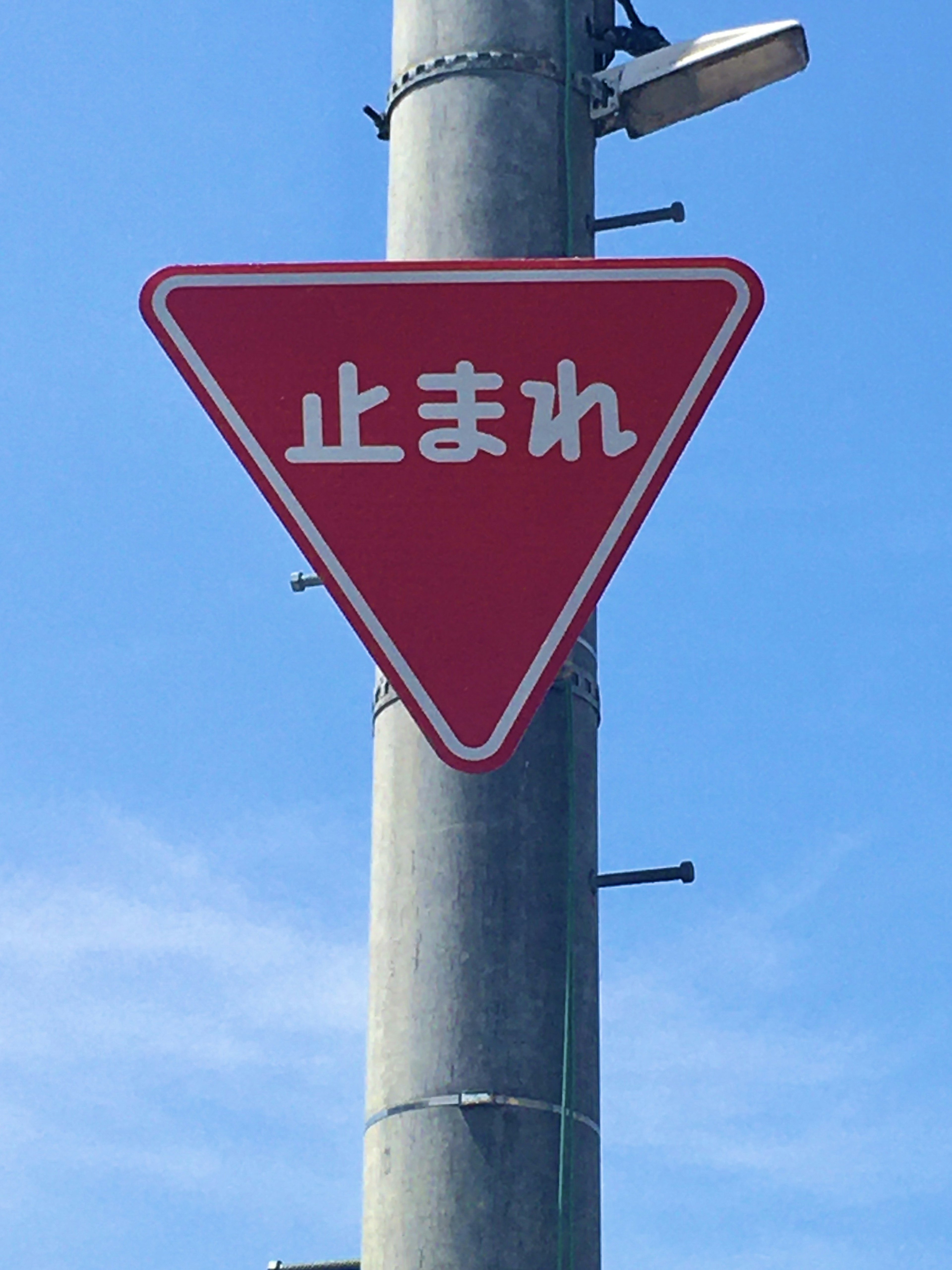 Red triangular stop sign with Japanese text on a pole against a blue sky