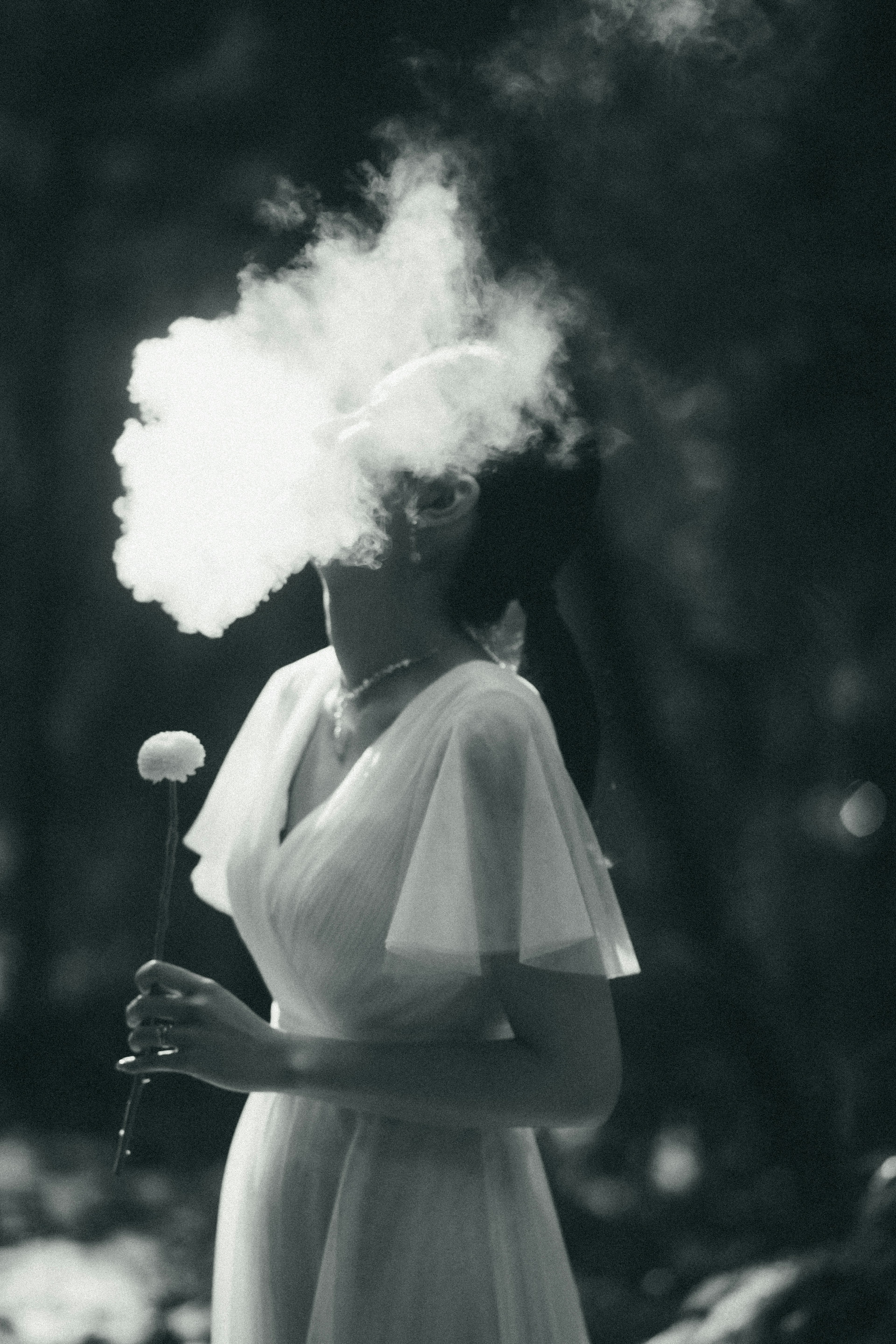 Une femme en robe blanche exhalant un nuage de fumée dans une image en noir et blanc