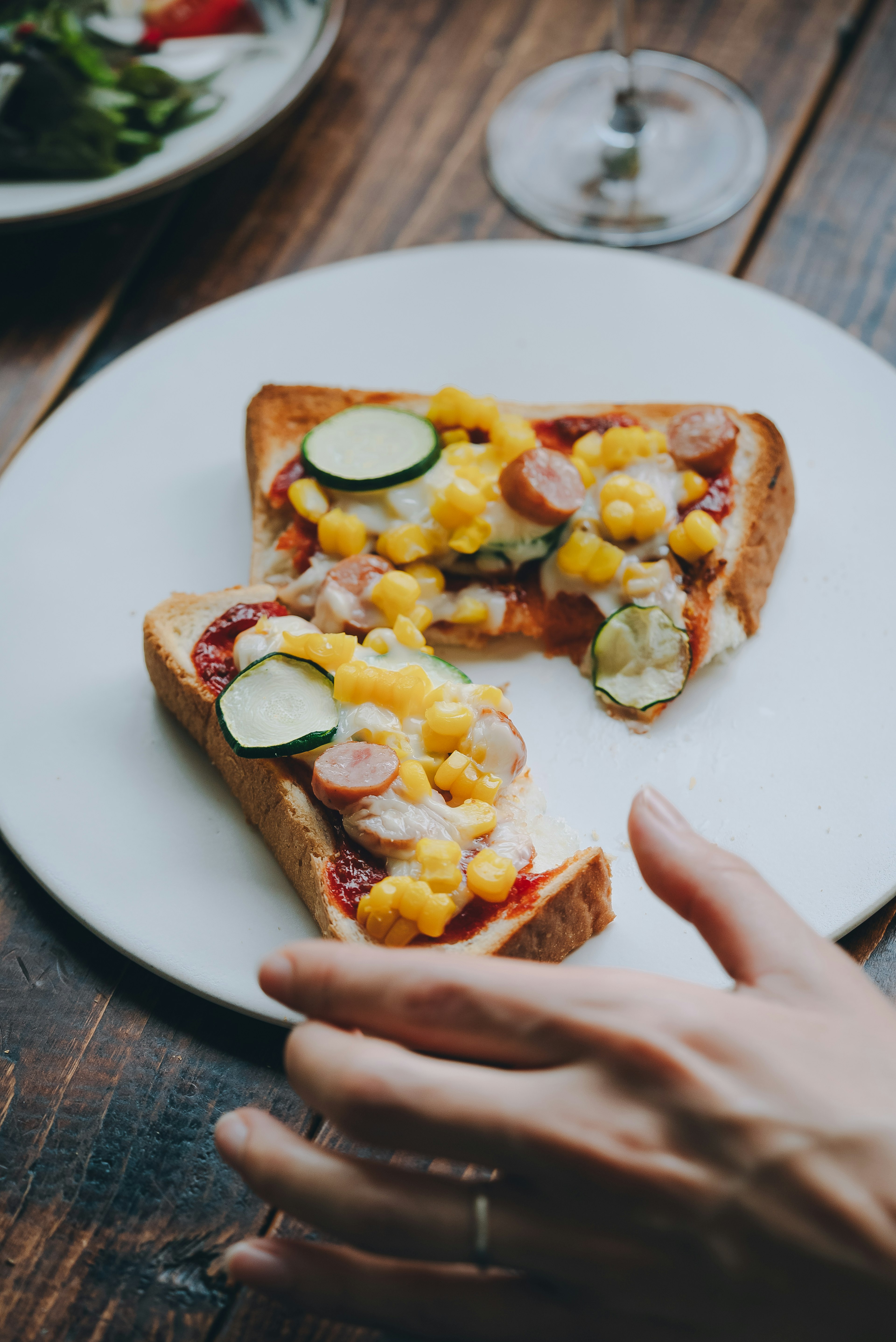 Cheese and vegetable toast served on a white plate with a hand