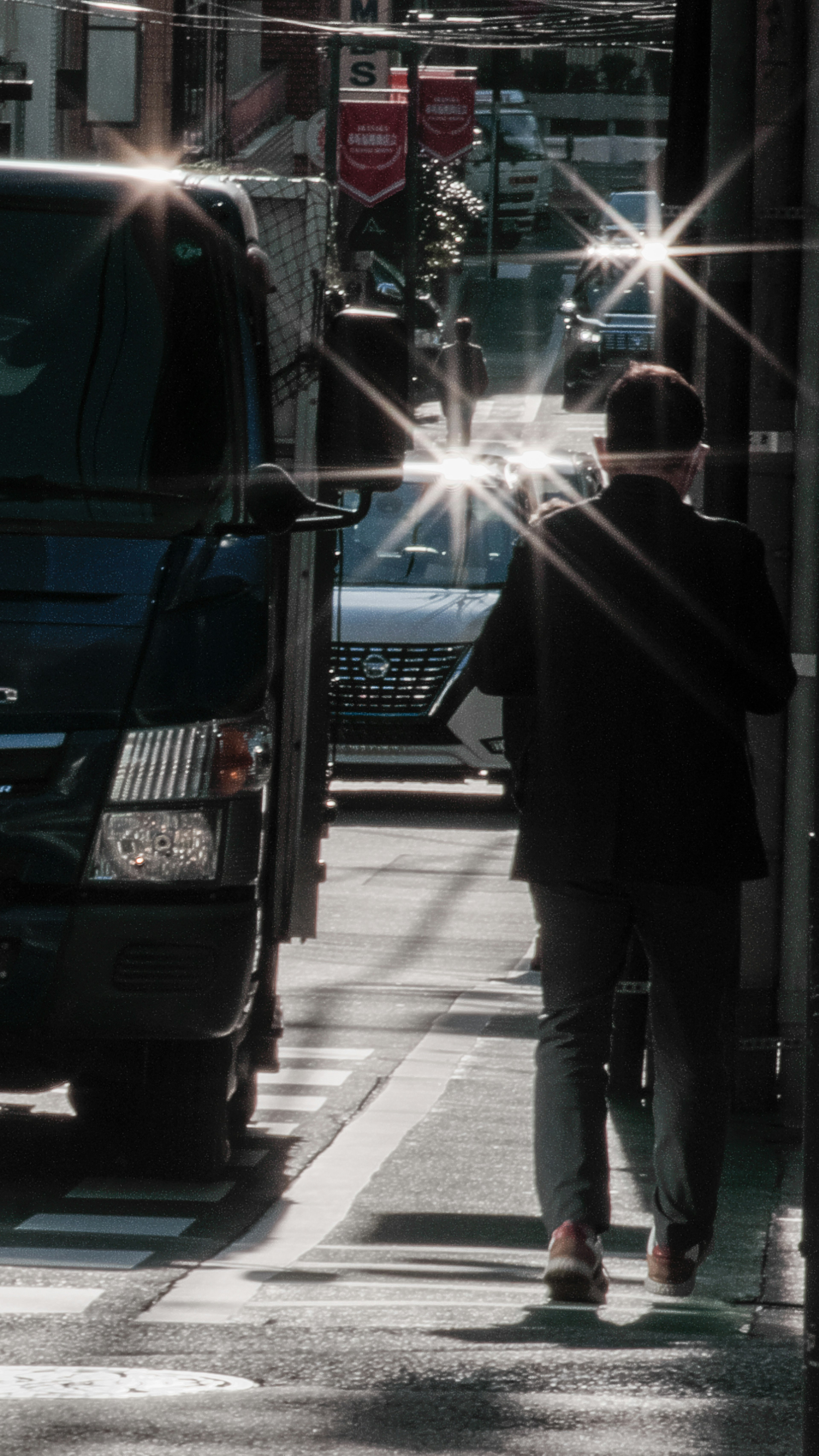 Ein Mann, der auf einer dunklen Straße mit funkelnden Scheinwerfern von Autos geht