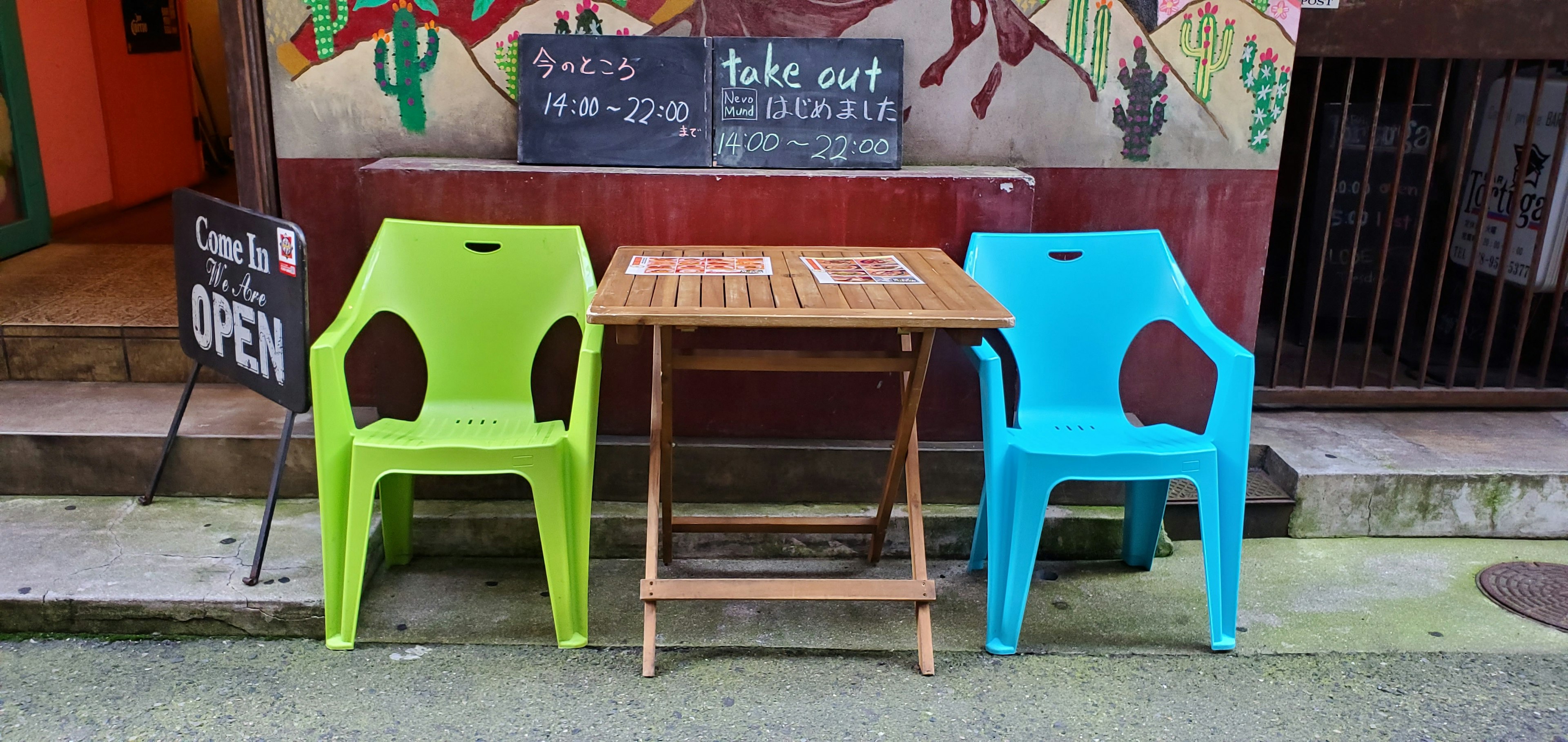 Green and blue plastic chairs in front of a wooden table at a café