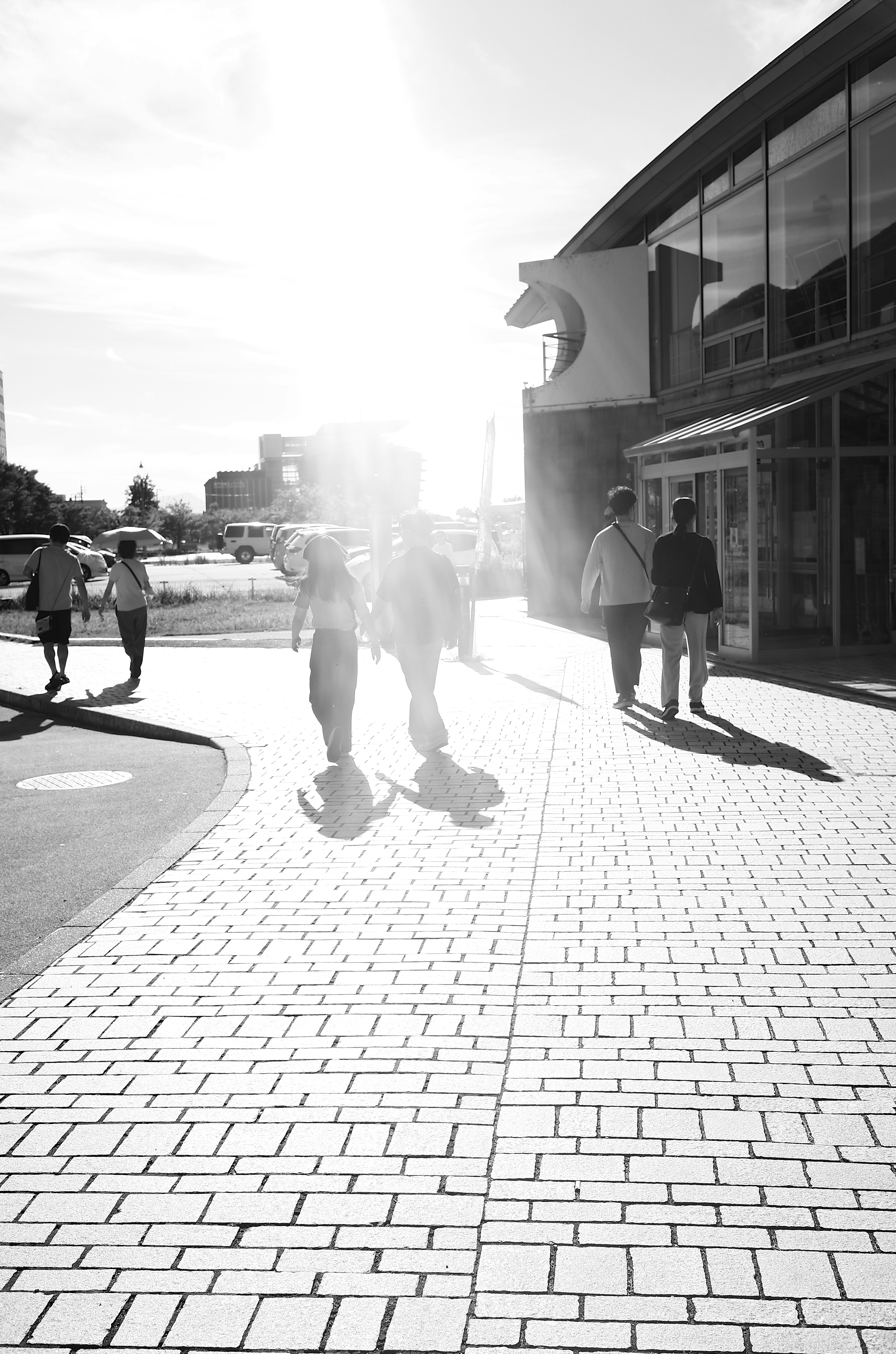 明るい日差しの中を歩く人々のシルエットが見える街の風景