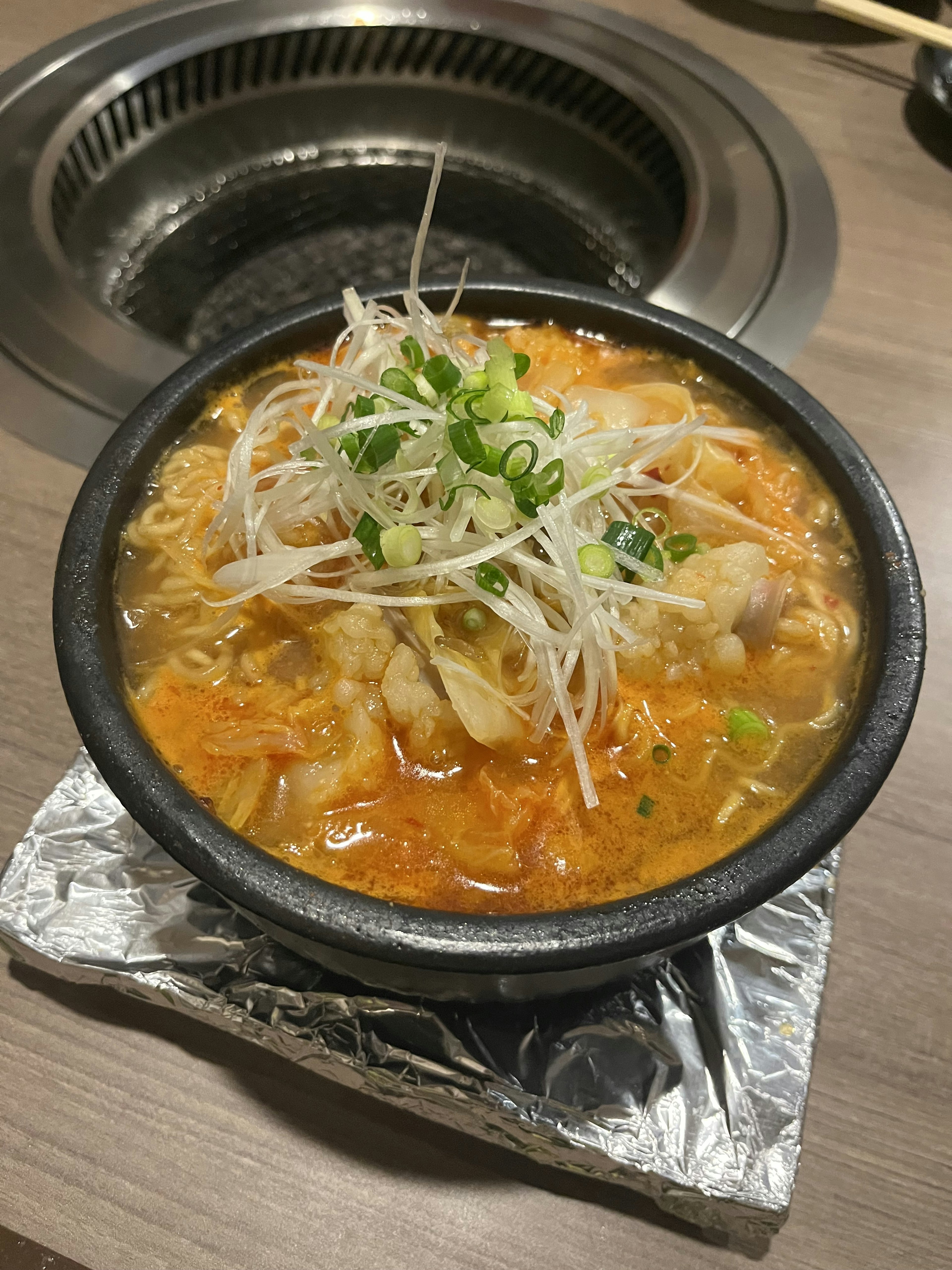 Zuppa calda con verdure e pollo in una pentola di pietra guarnita con cipollotti affettati