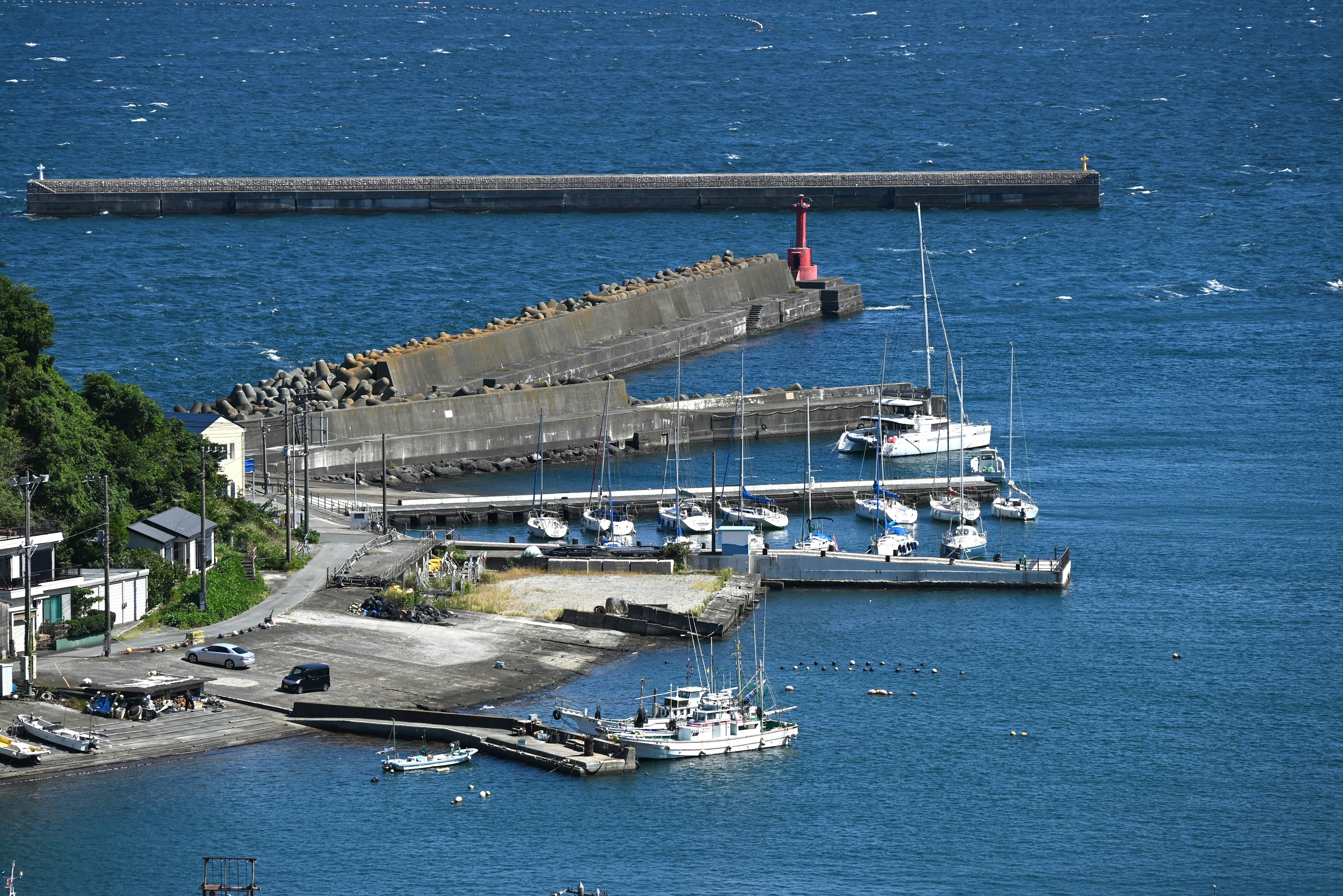 Una escena de puerto con agua azul y yates con un muelle y un faro cercanos