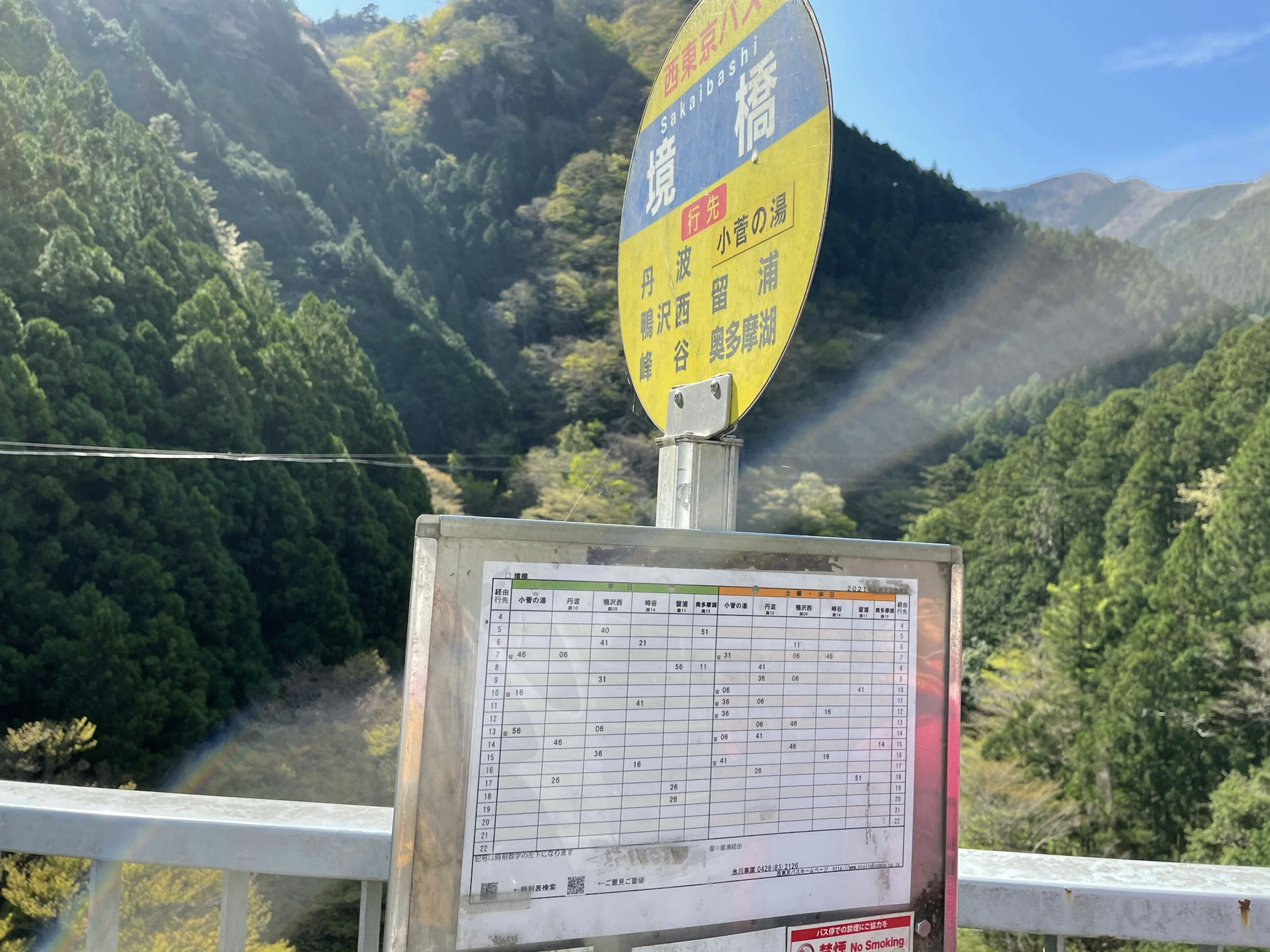 Señal de parada de autobús con tabla de horarios frente a montañas verdes