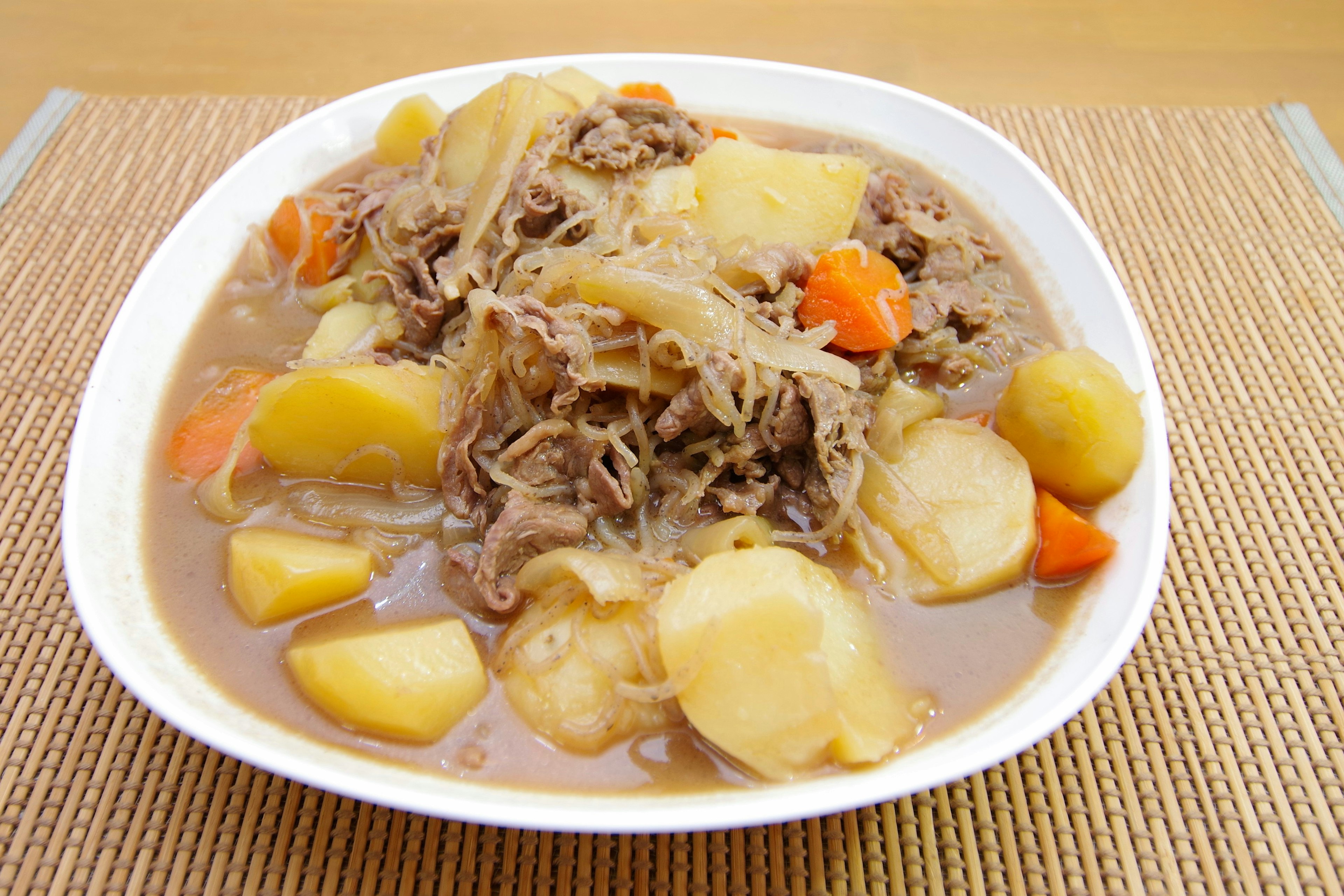 Un piatto bianco pieno di uno stufato sostanzioso di carne e verdure