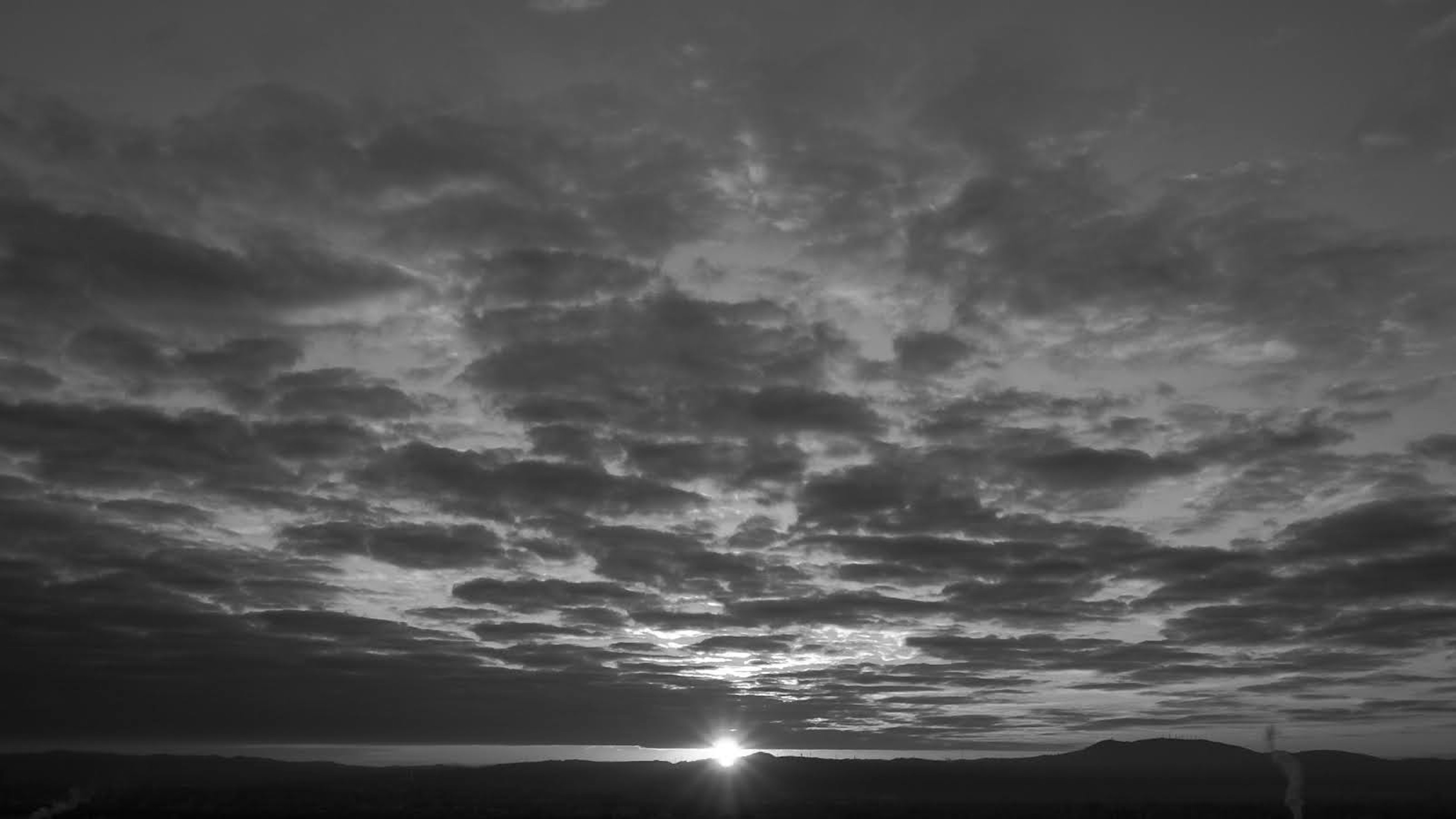 Black and white image of the sun setting behind a cloudy sky