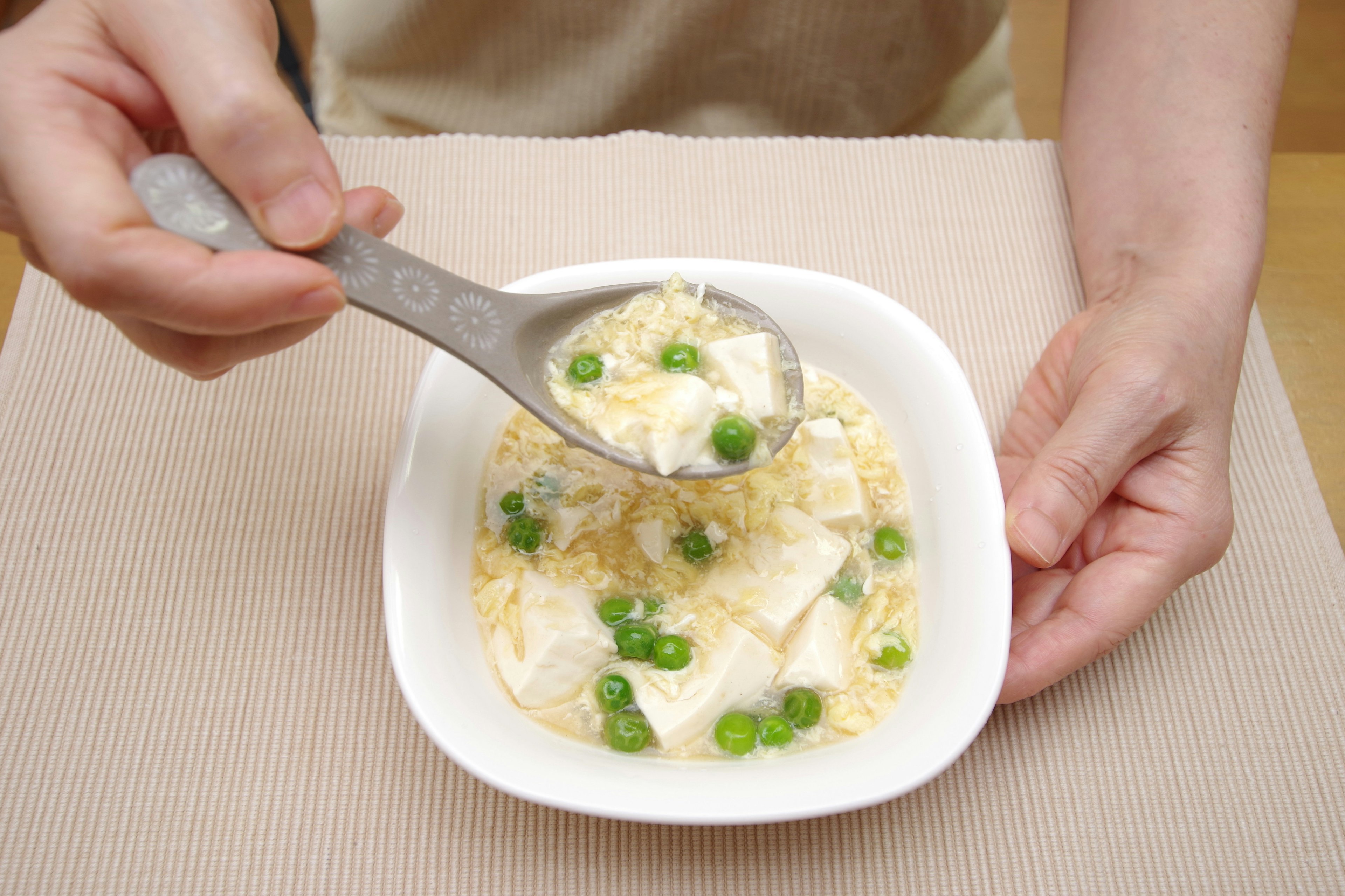 Mani che servono tofu e piselli con un cucchiaio