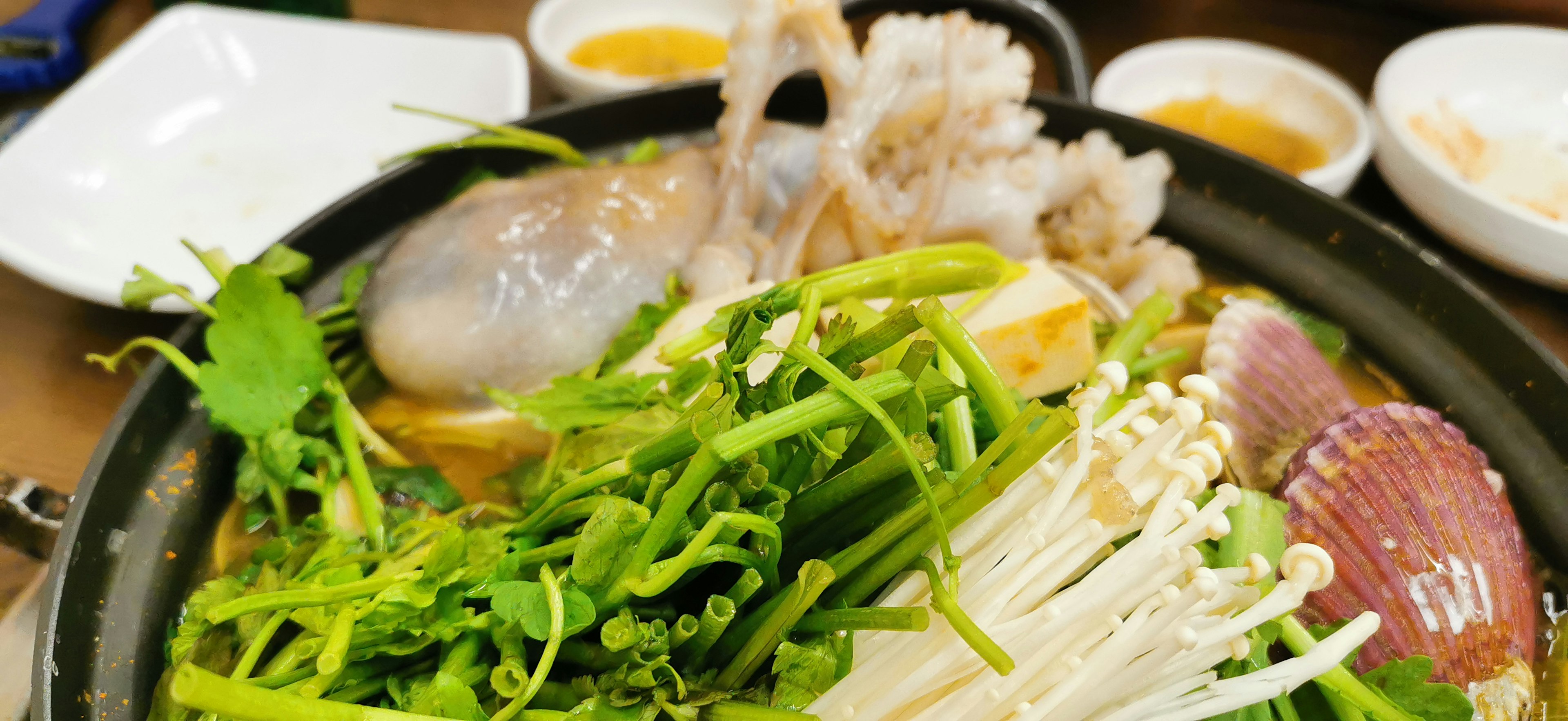 A hot pot filled with fresh vegetables and seafood ingredients