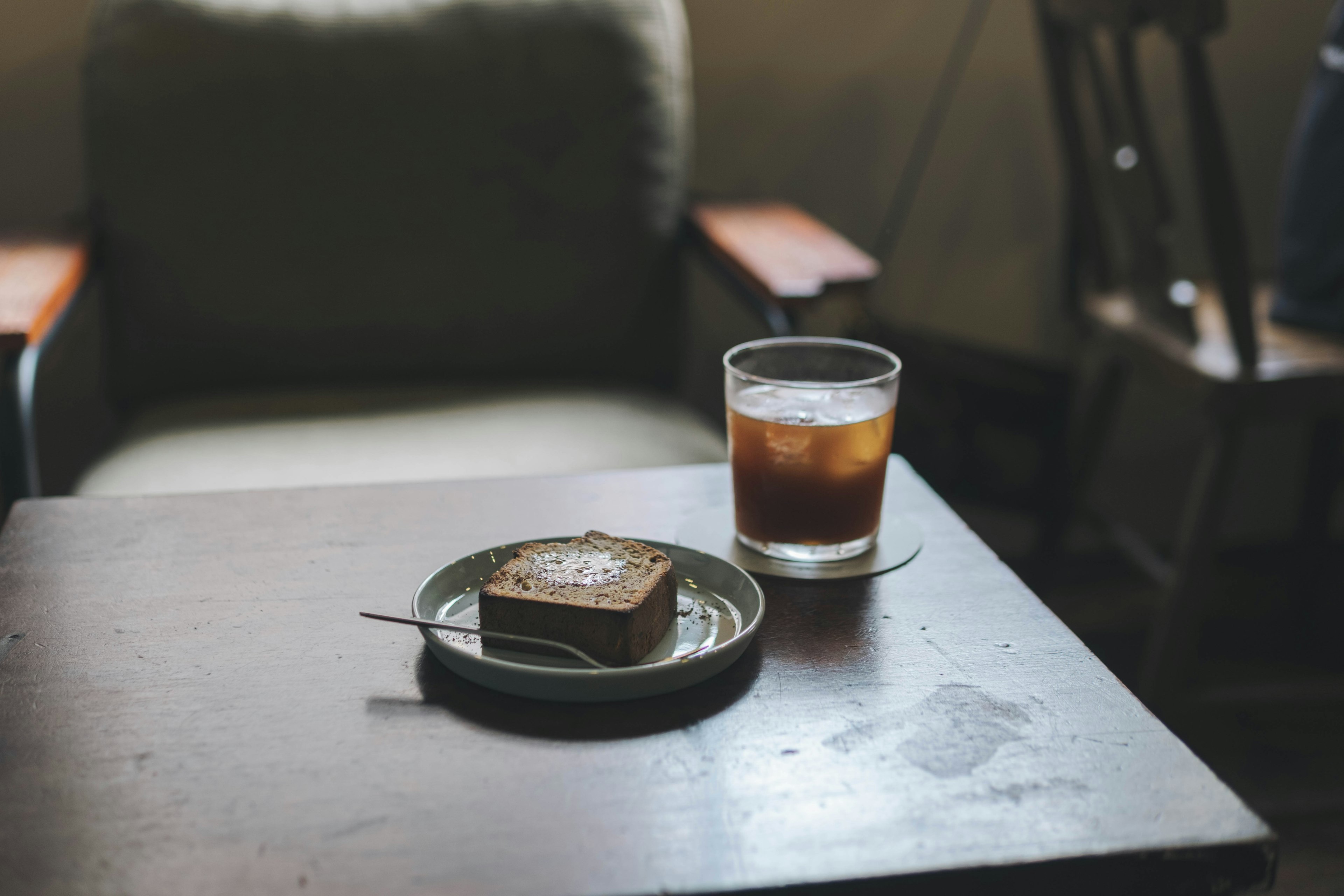 A wooden table featuring a glass of iced coffee and a dessert on a plate