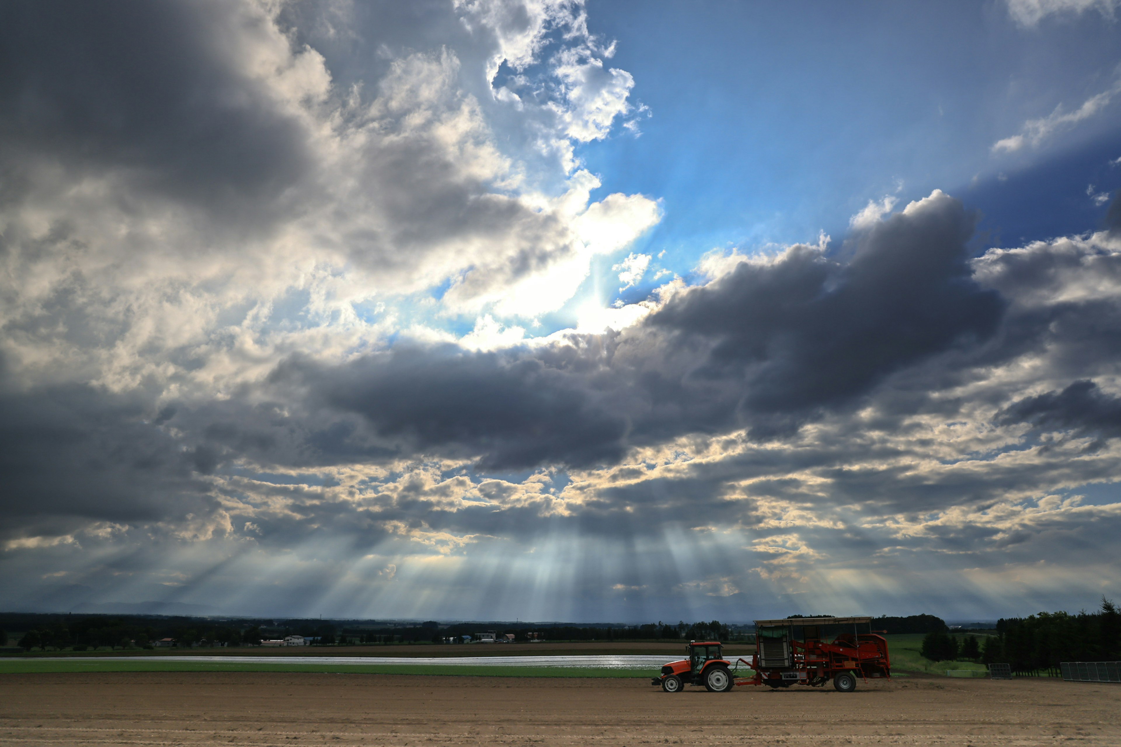 Tractor en tierras agrícolas bajo un cielo dramático con rayos de sol