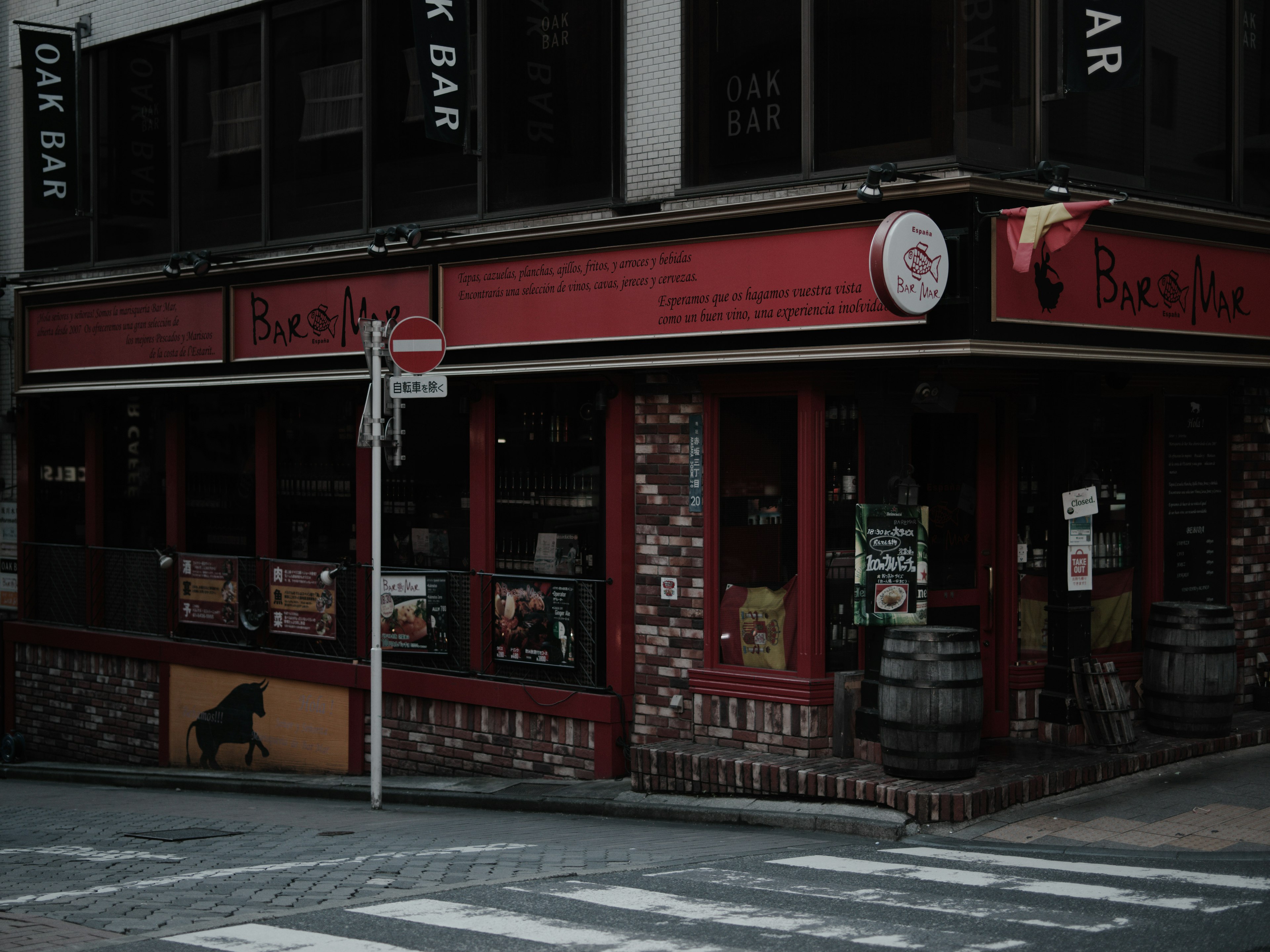 赤い看板の居酒屋風の建物に木製の樽が並ぶ