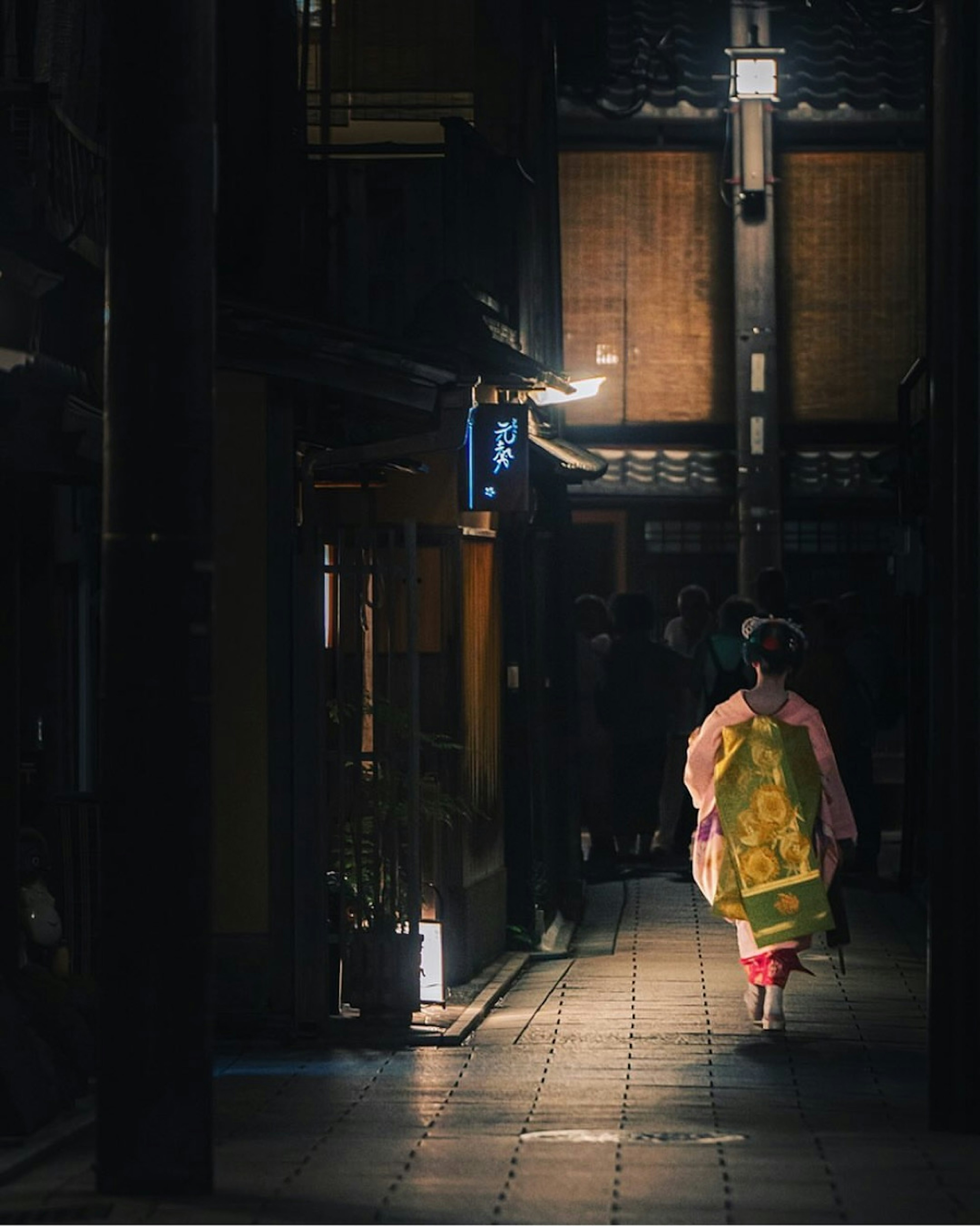 Frau im Kimono, die durch eine Nachtstraße geht