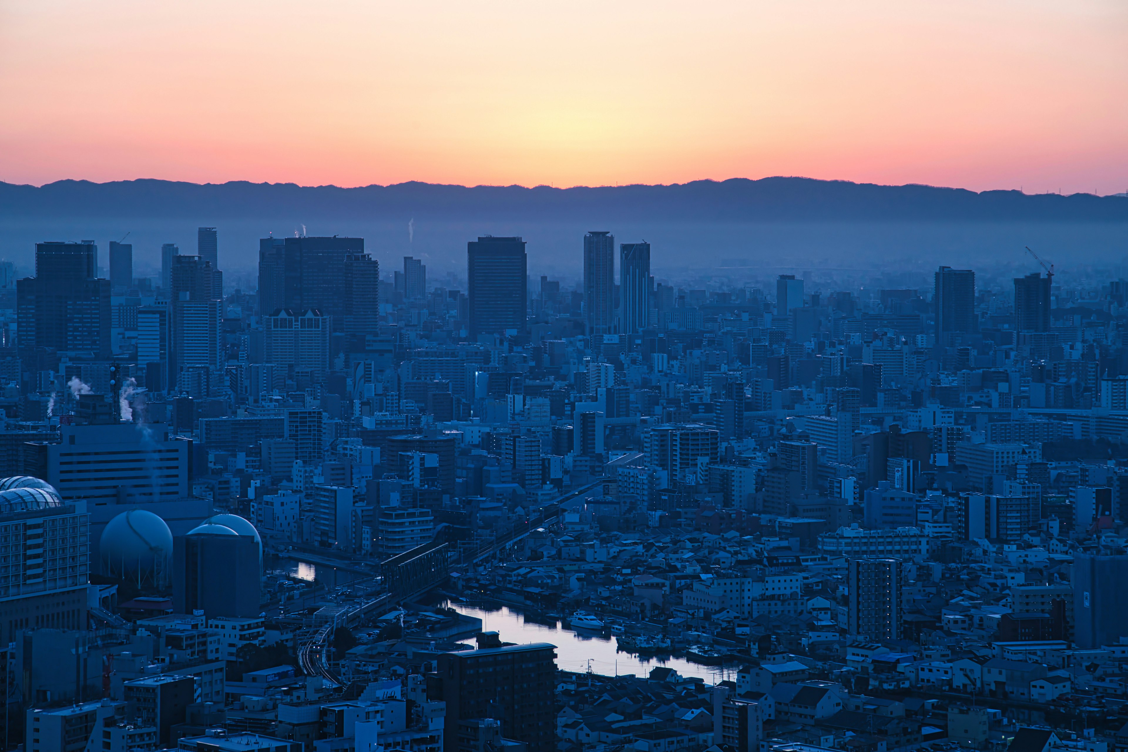 Silhouette of skyscrapers against a sunset with a river in the foreground