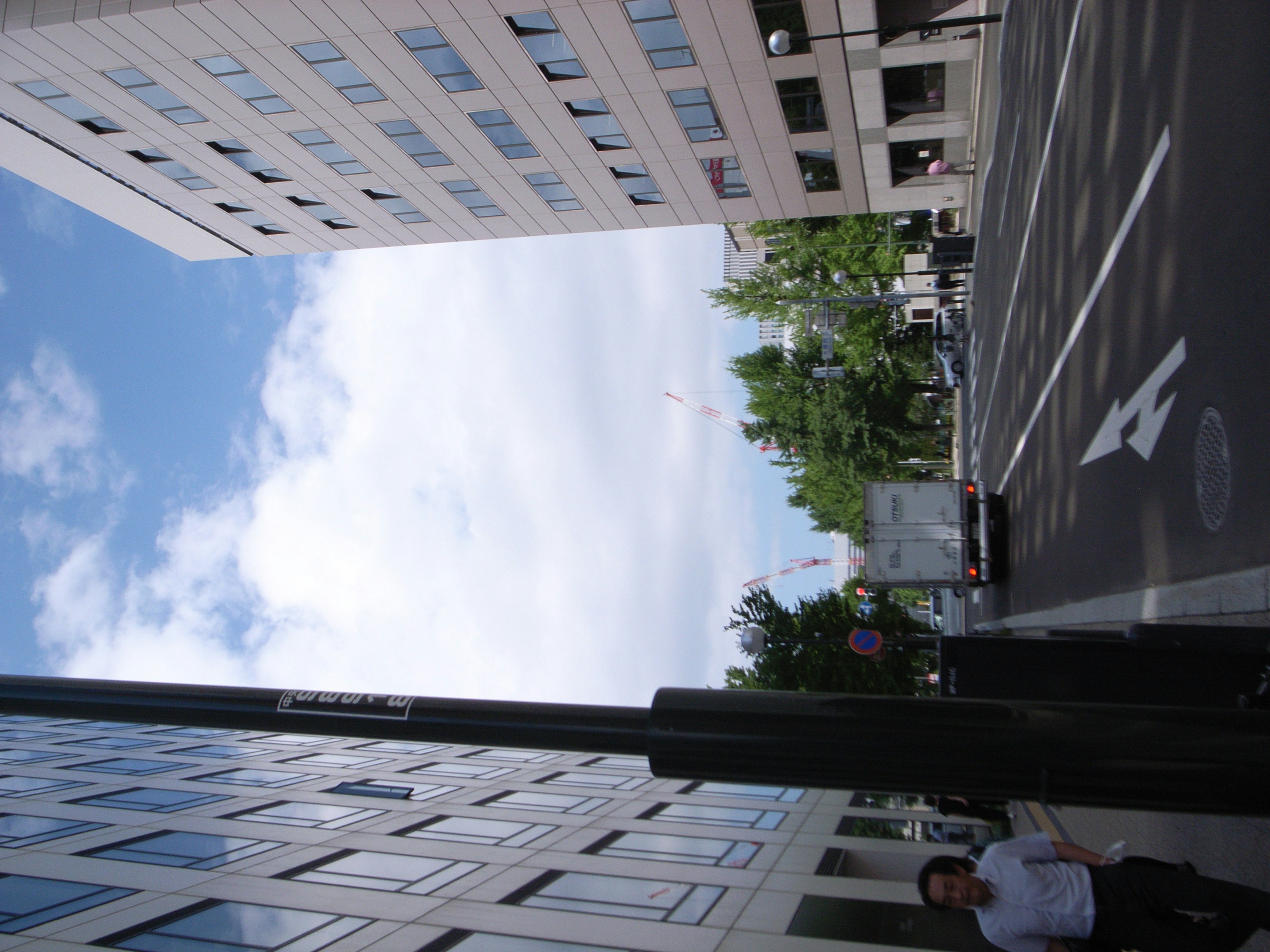 青空と雲を背景にした現代的なビルと街路の風景