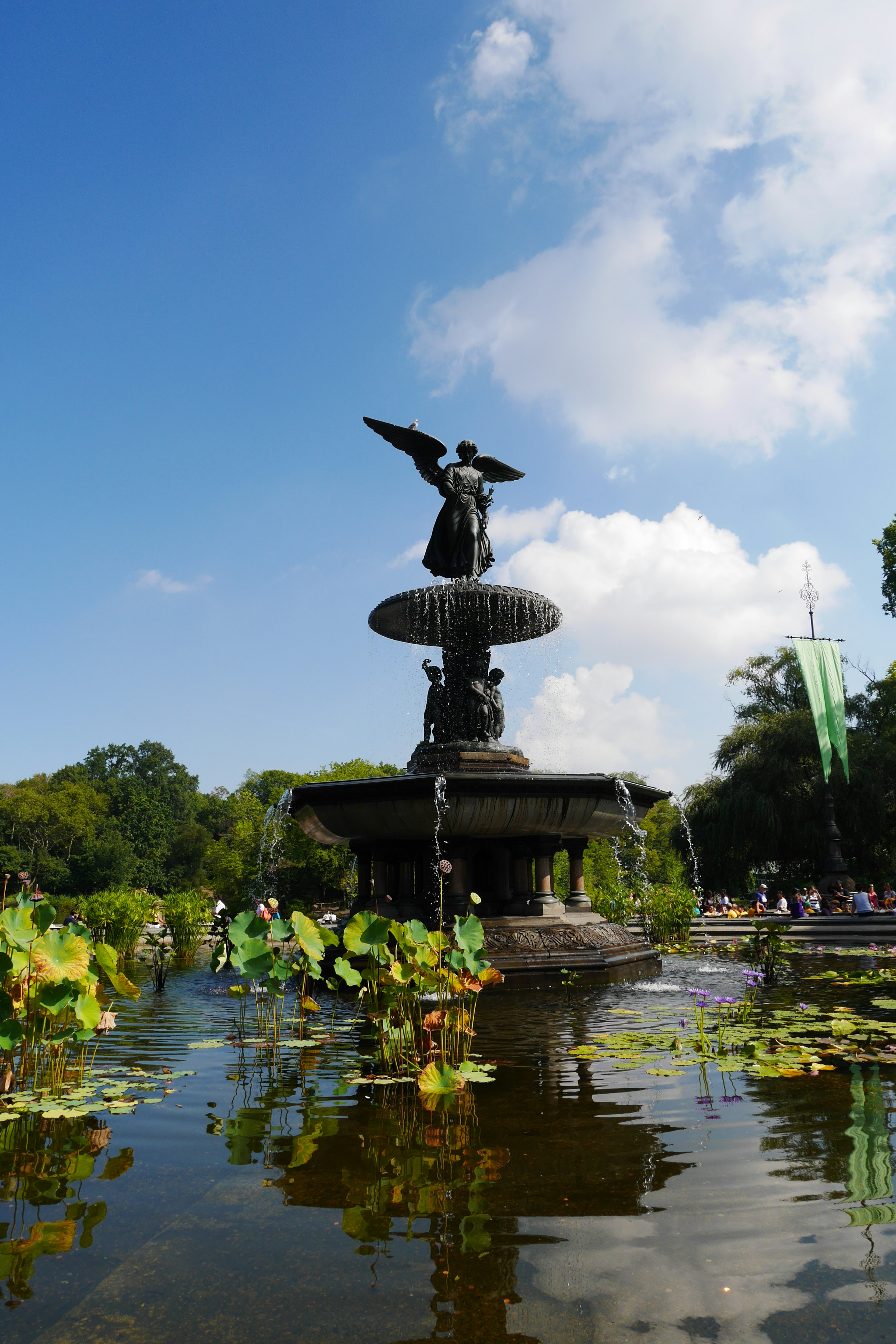 Pemandangan indah Air Mancur Bethesda di Central Park yang memantul di atas air langit biru dan awan dikelilingi oleh vegetasi subur