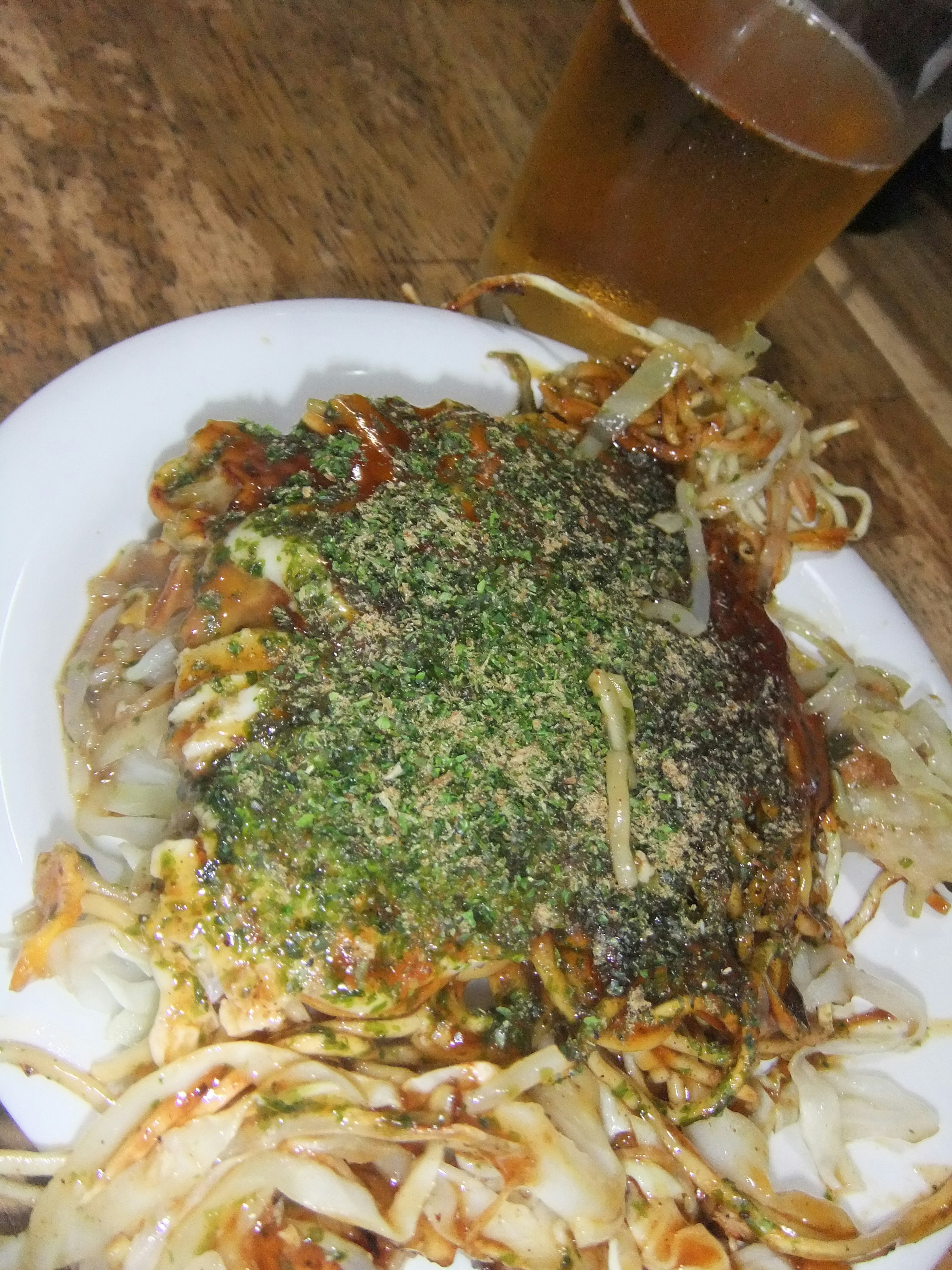 Sepiring okonomiyaki yang ditaburi bumbu hijau dan segelas bir