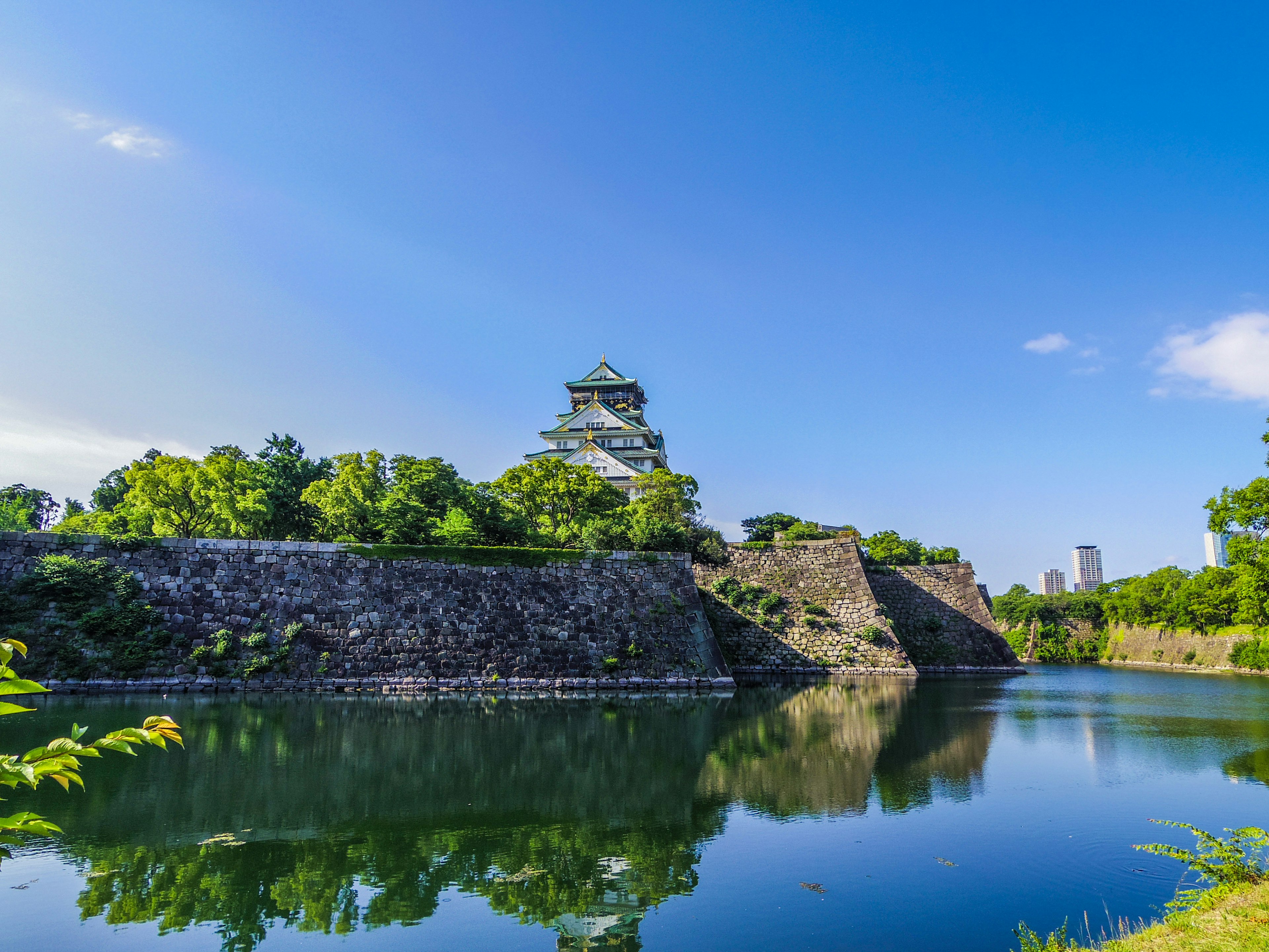 Kastil Jepang dikelilingi oleh pepohonan dan memantulkan diri di air tenang