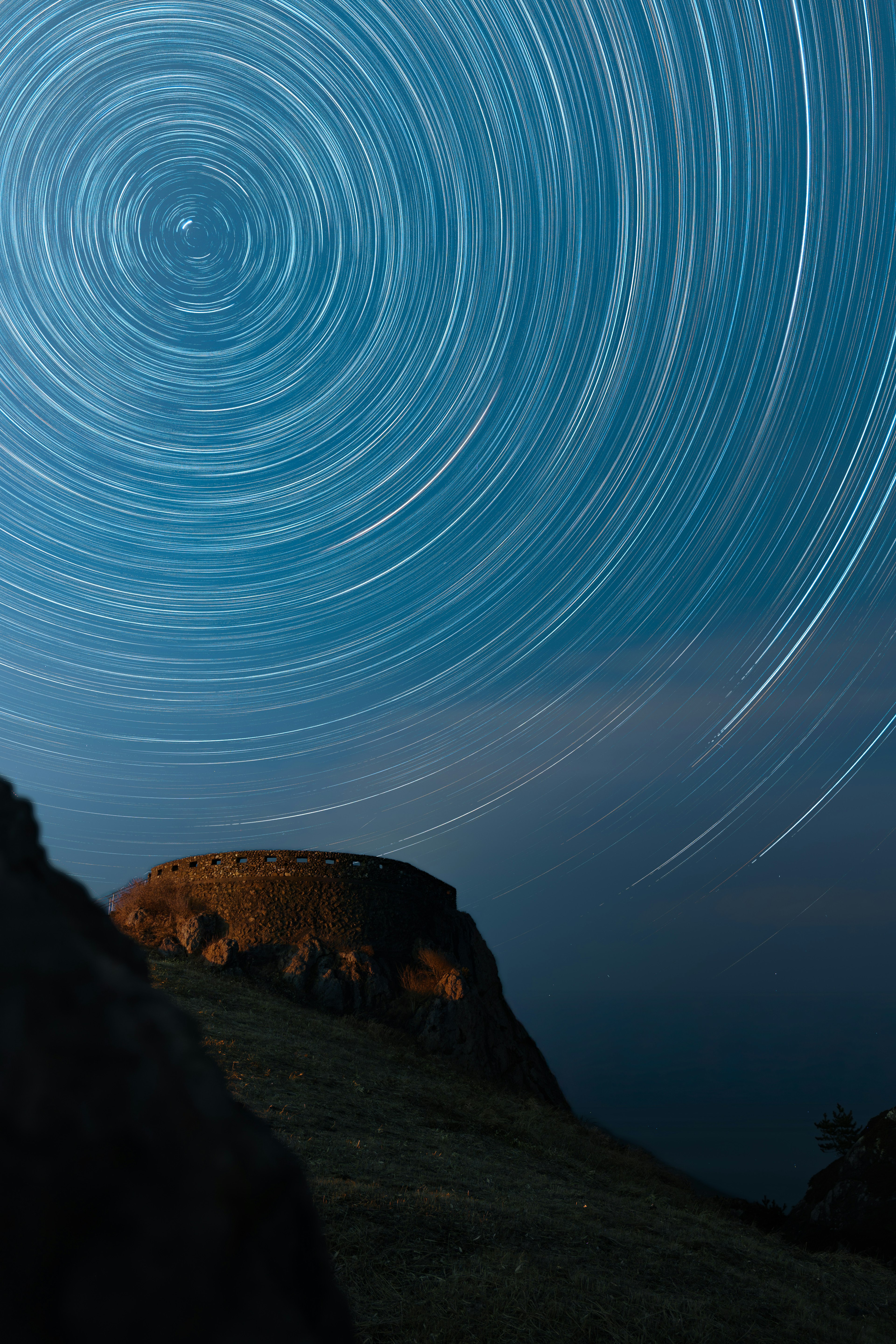 Night sky with star trails above a silhouetted hill