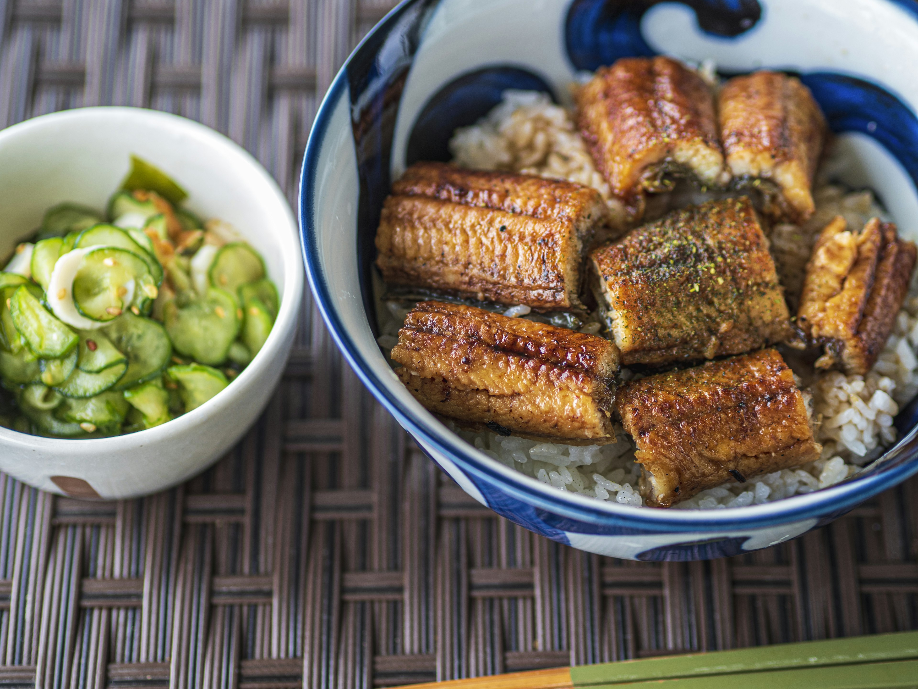 米飯上放著烤鰻魚，旁邊有黃瓜沙拉