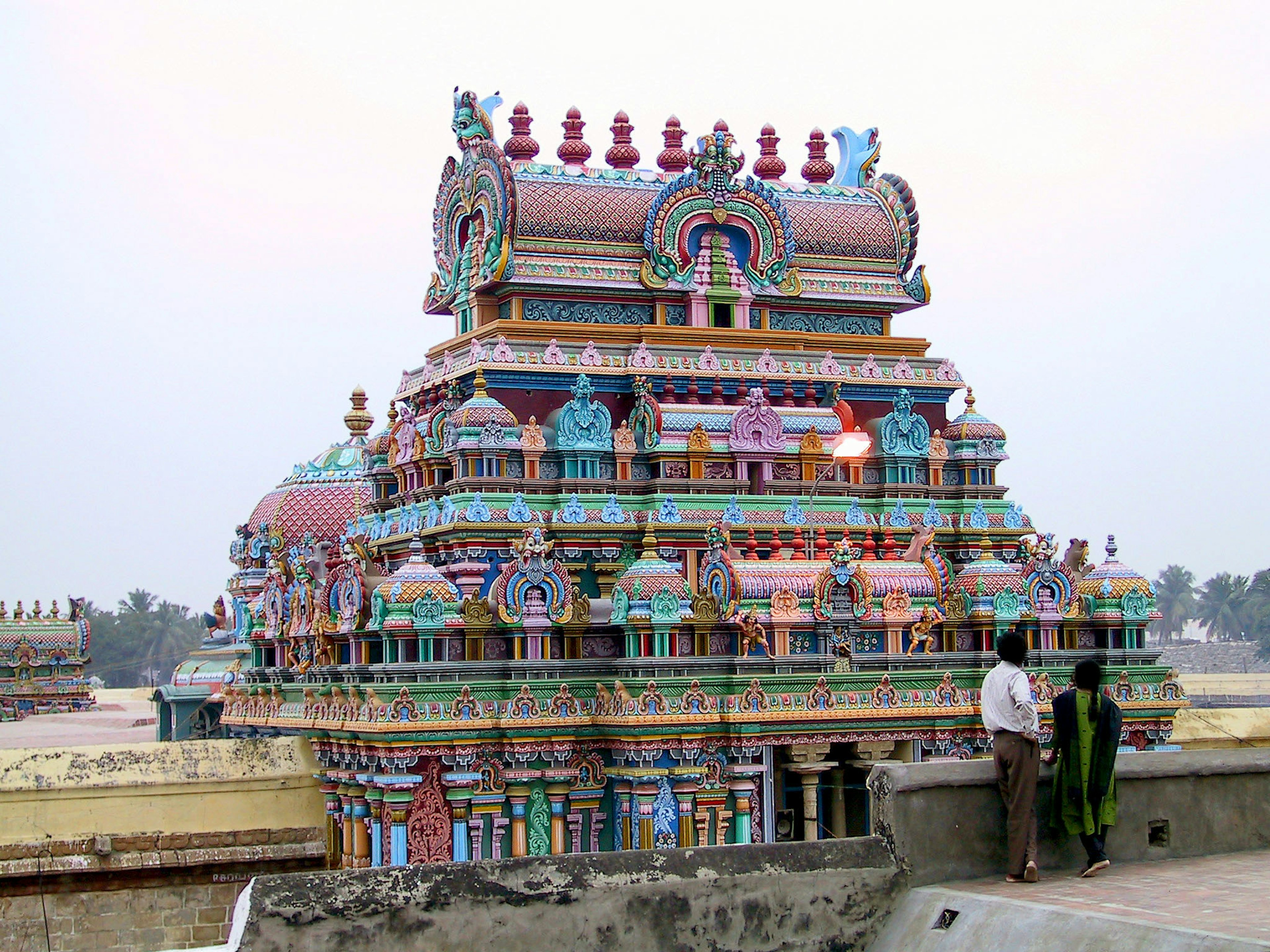 Vibrantly decorated South Indian temple exterior under twilight with two people standing nearby