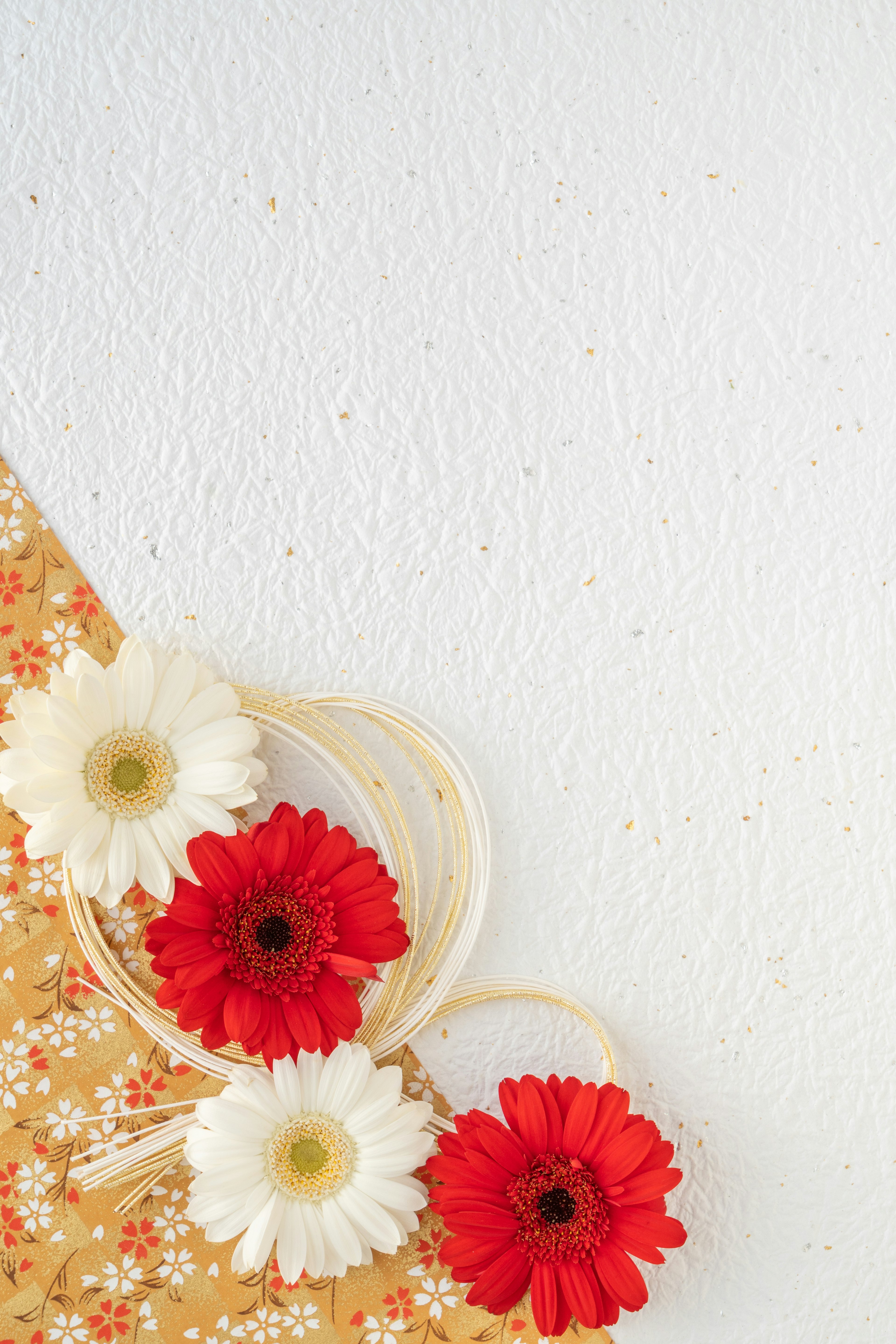 Flores de gerbera rojas y blancas dispuestas sobre una tela floral amarilla con fondo blanco