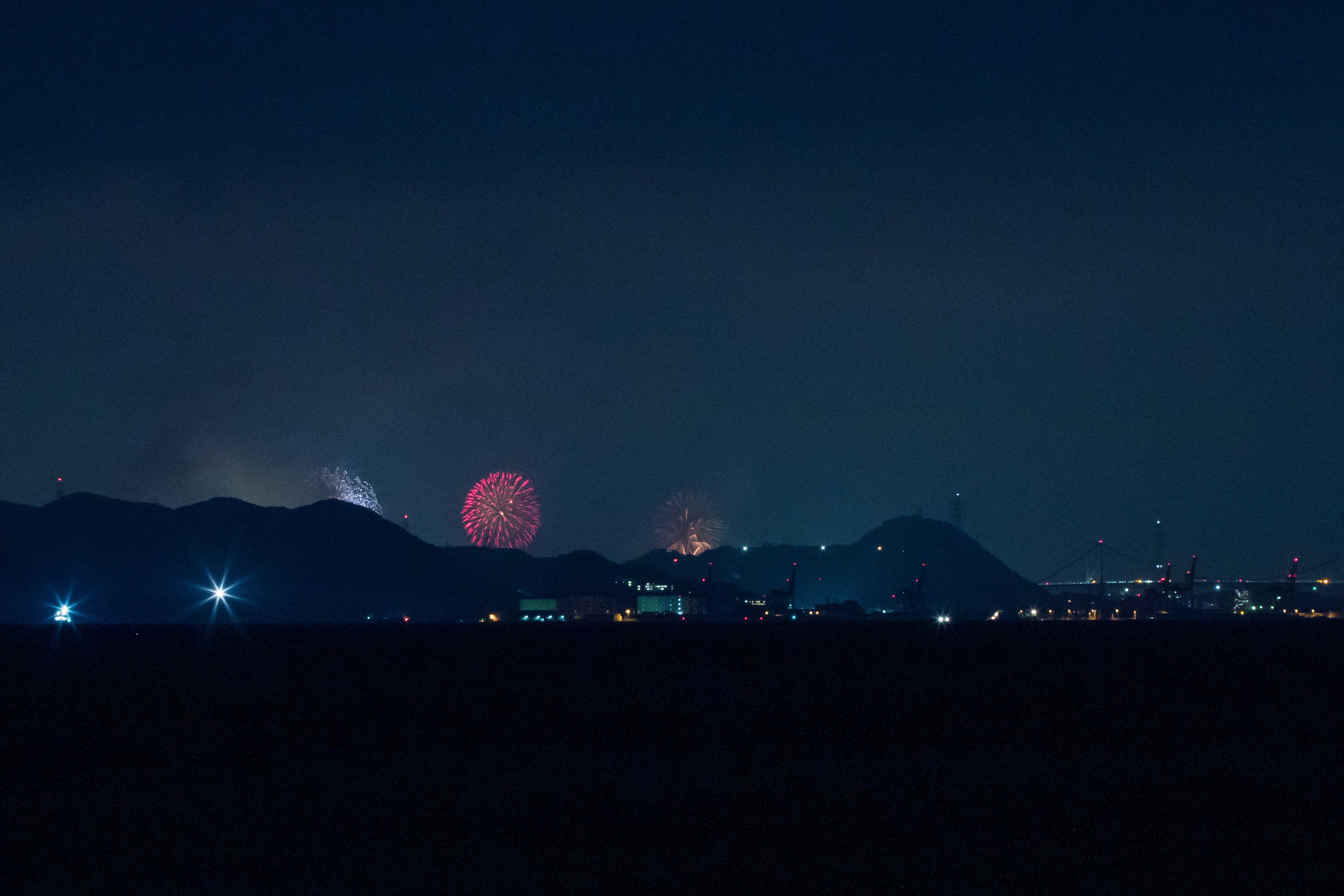 夜空に浮かぶ花火と山のシルエットが印象的な風景