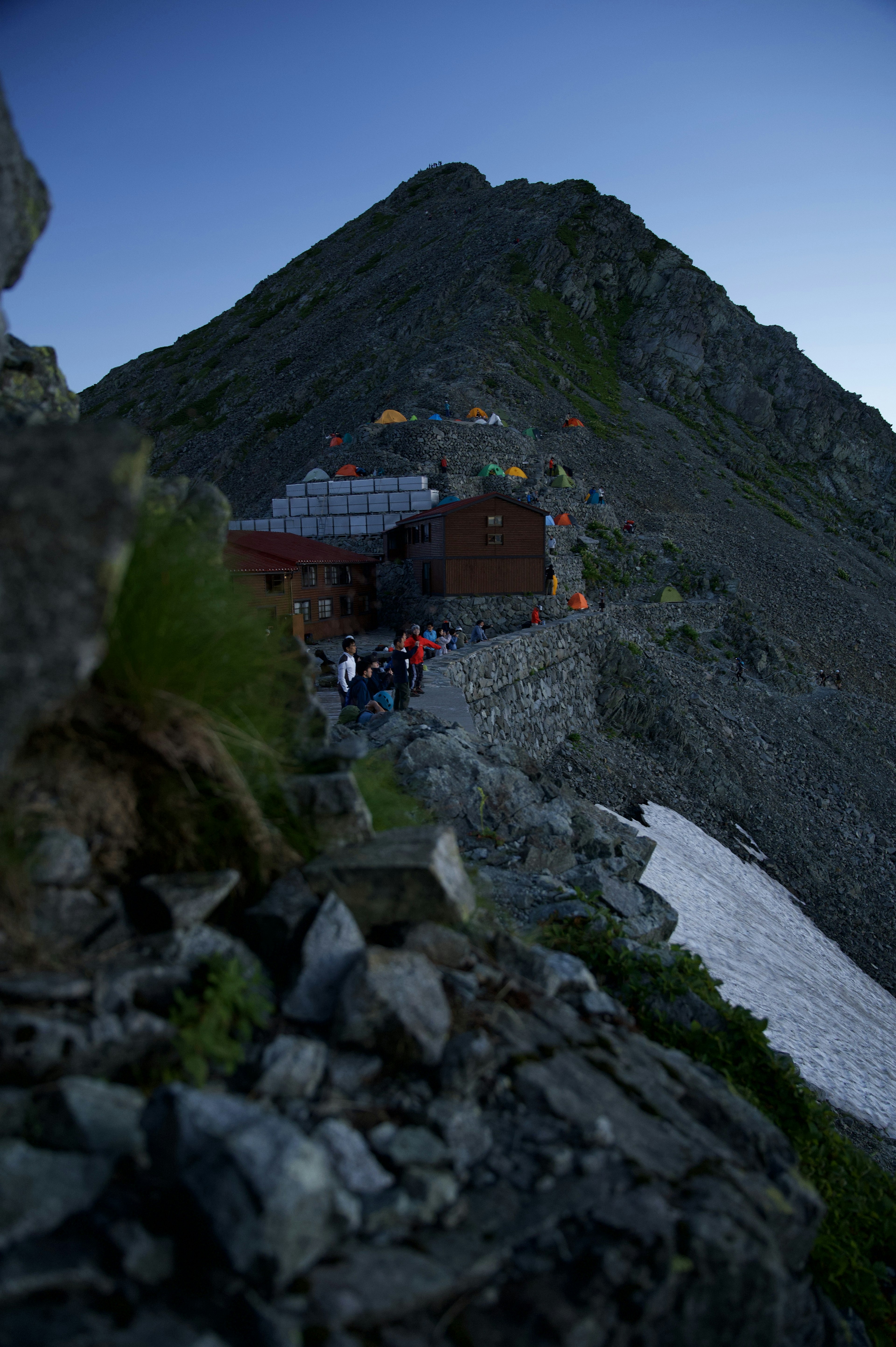 山の斜面に建つ小屋と登山者たちの姿が見える風景