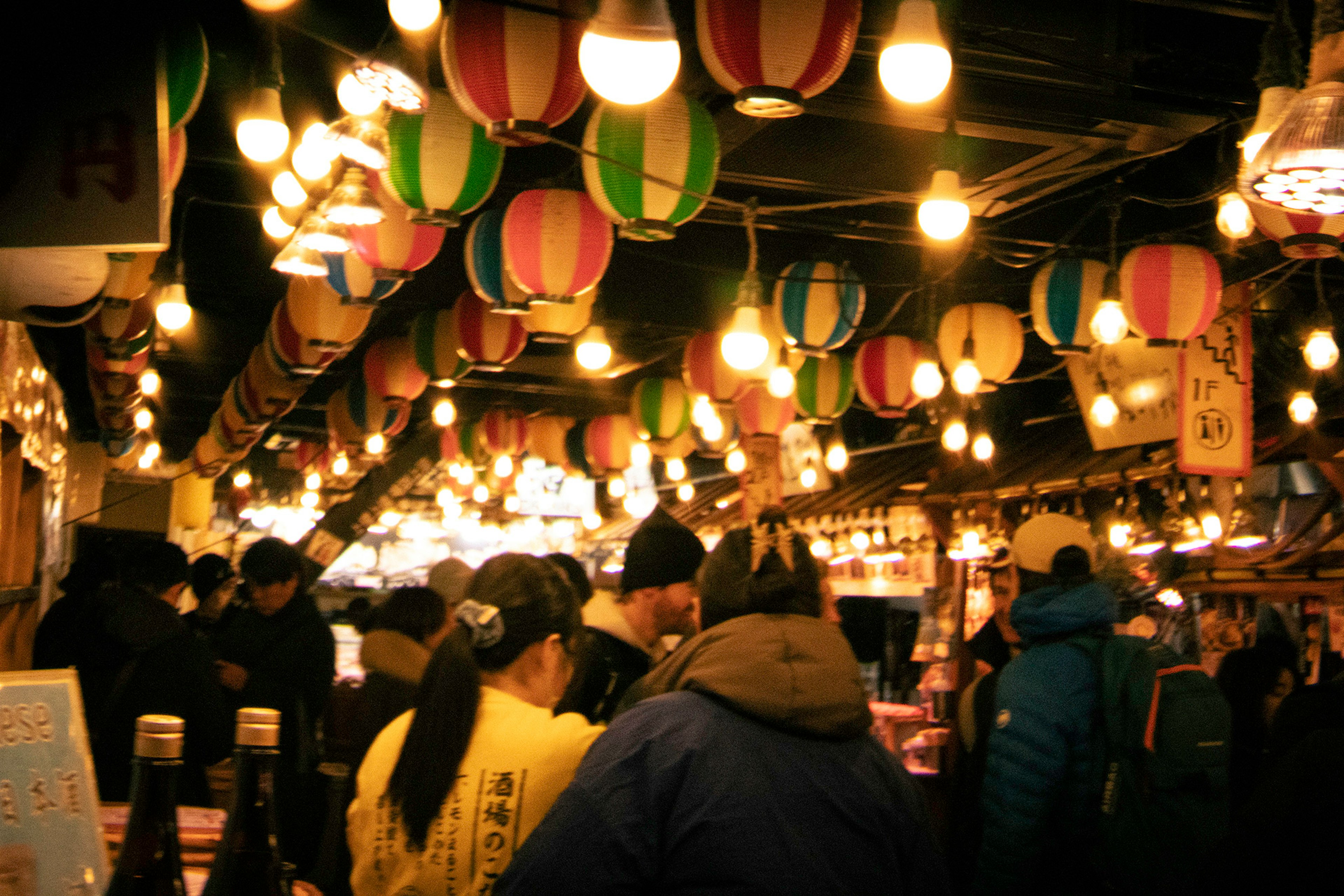 A lively market interior with colorful lanterns hanging and crowds of people