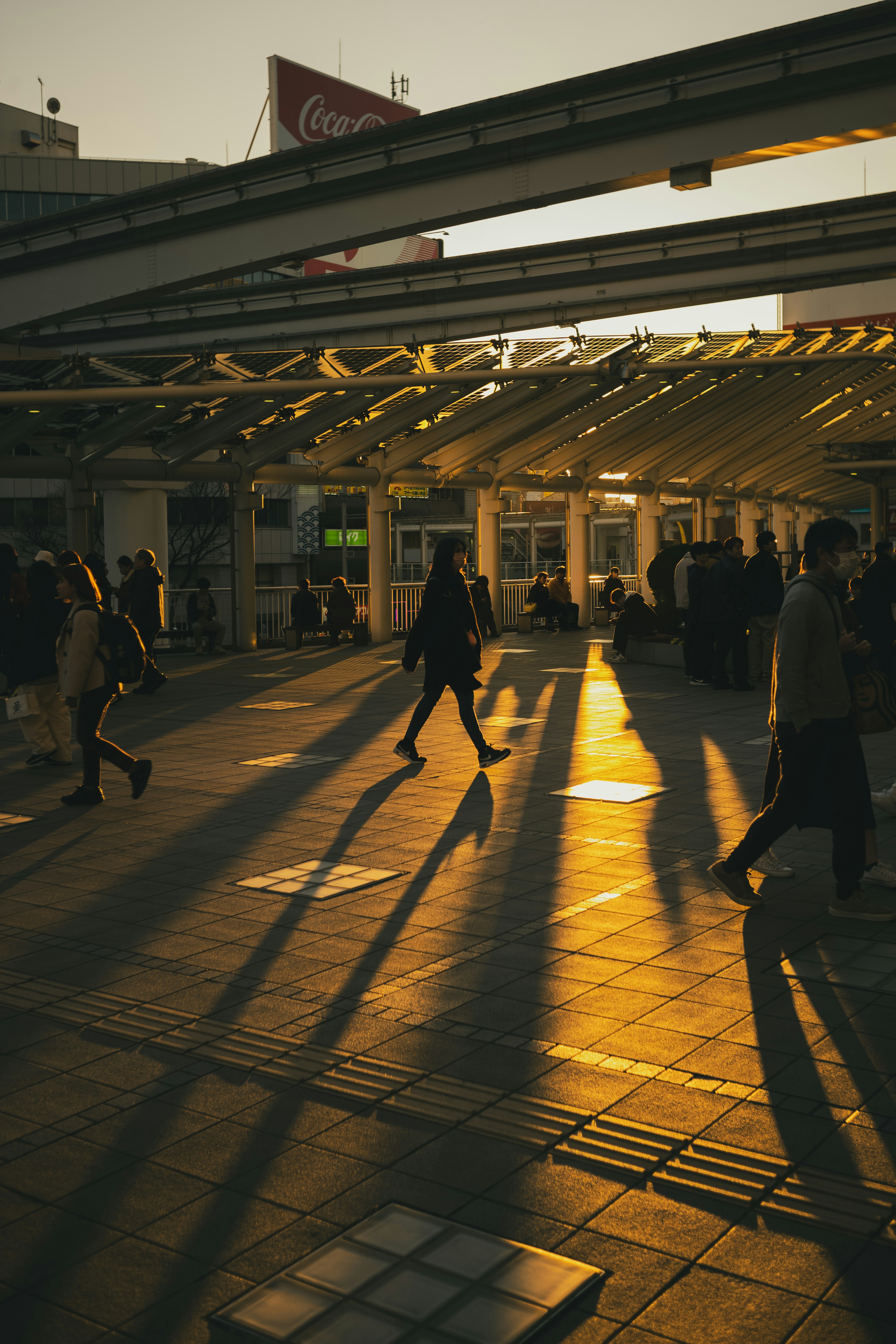 夕暮れの駅前で影を落としながら歩く人々