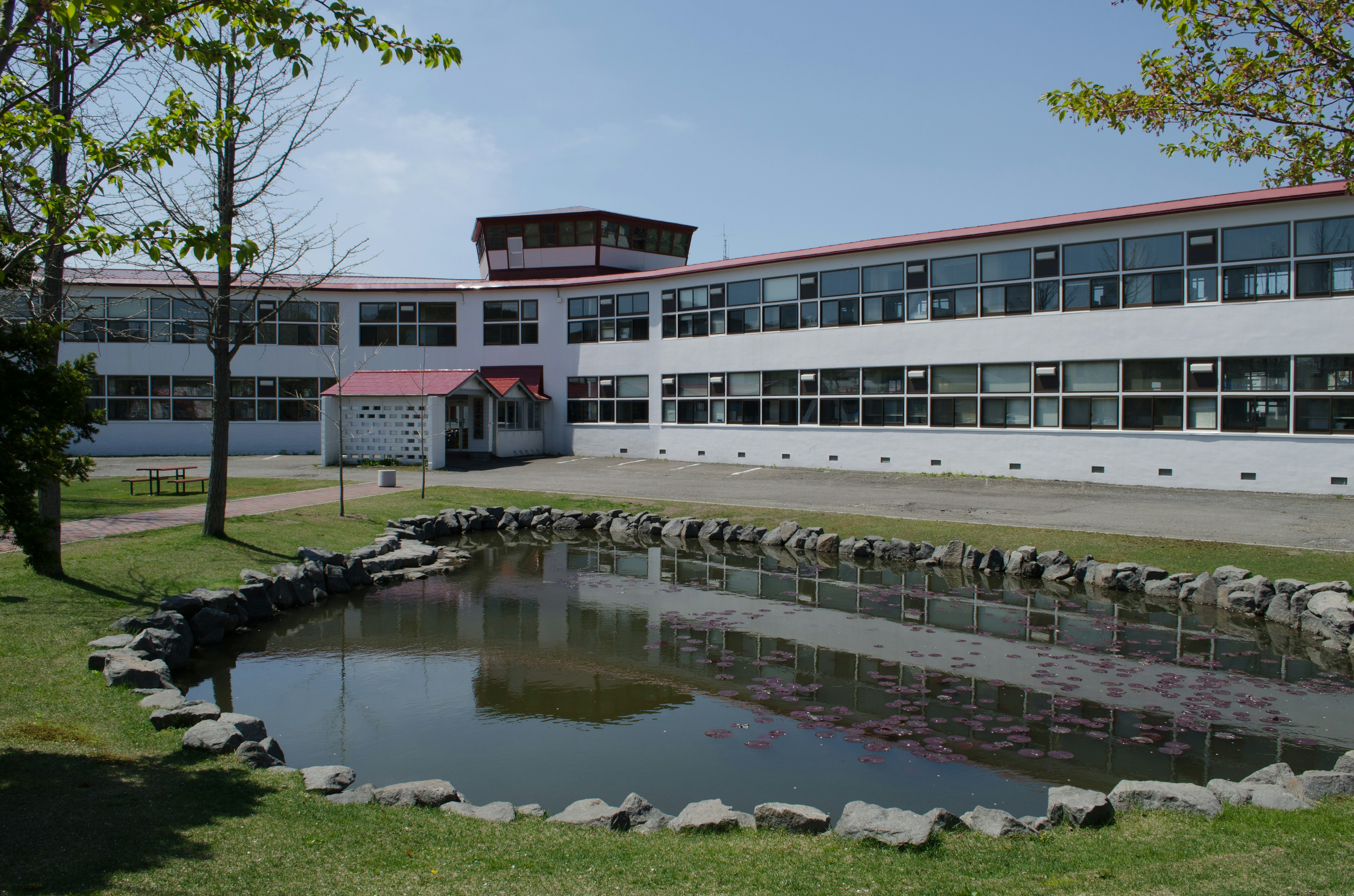 Bâtiment scolaire avec un étang, ciel bleu et arbres verts