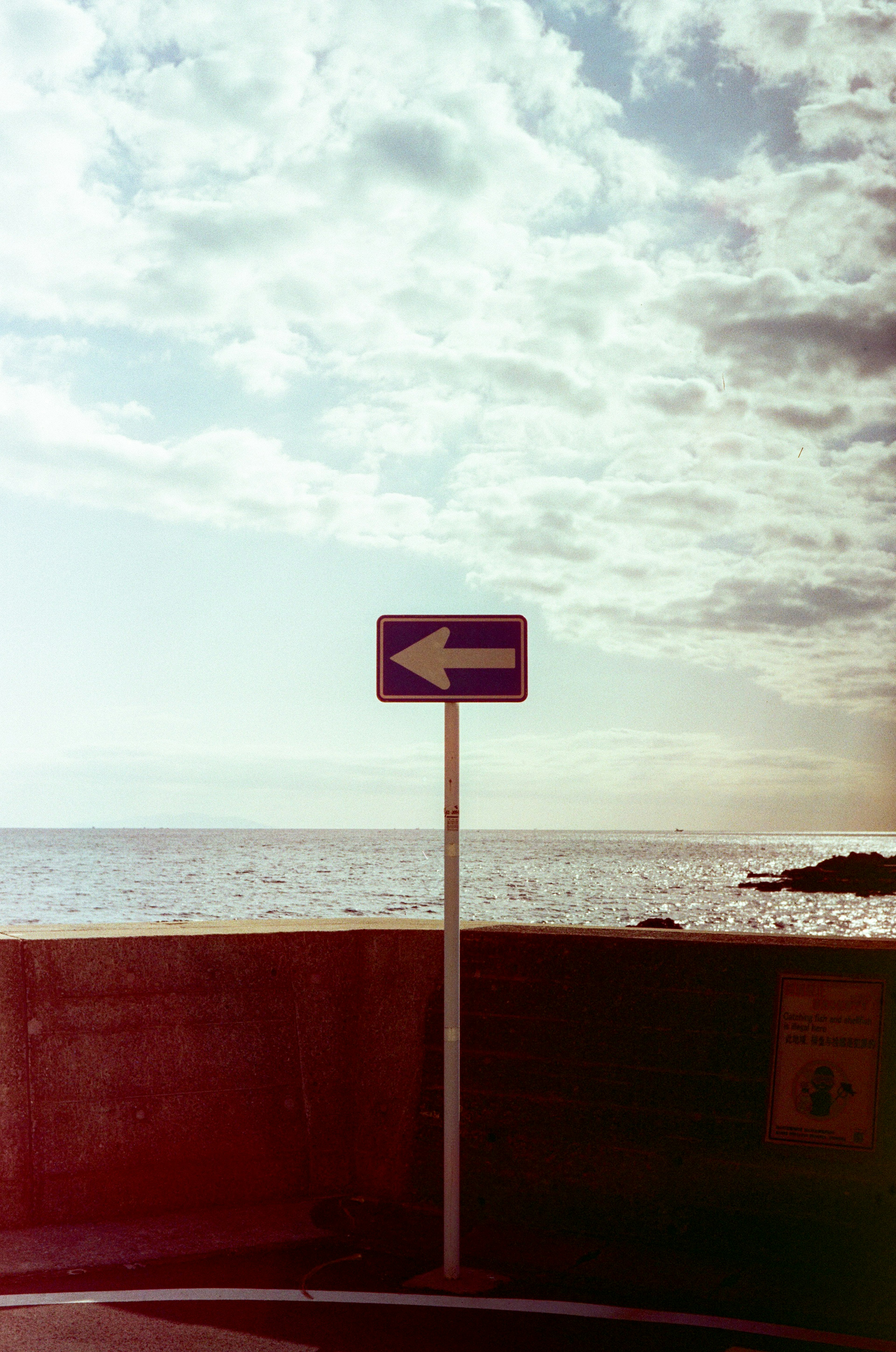 Un panneau fléché à gauche devant un ciel bleu et la mer