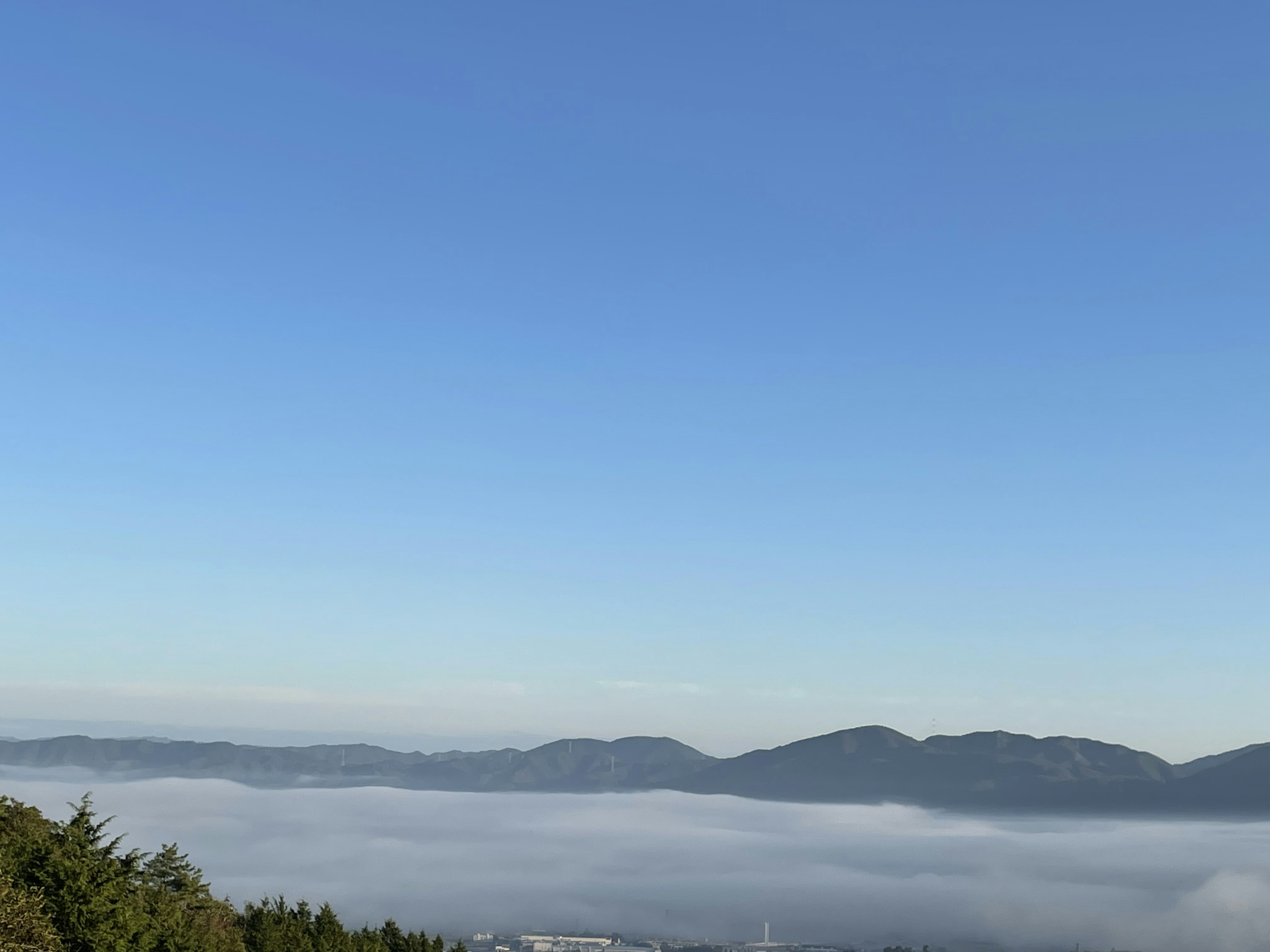 Paesaggio montano con un mare di nuvole sotto un cielo blu chiaro